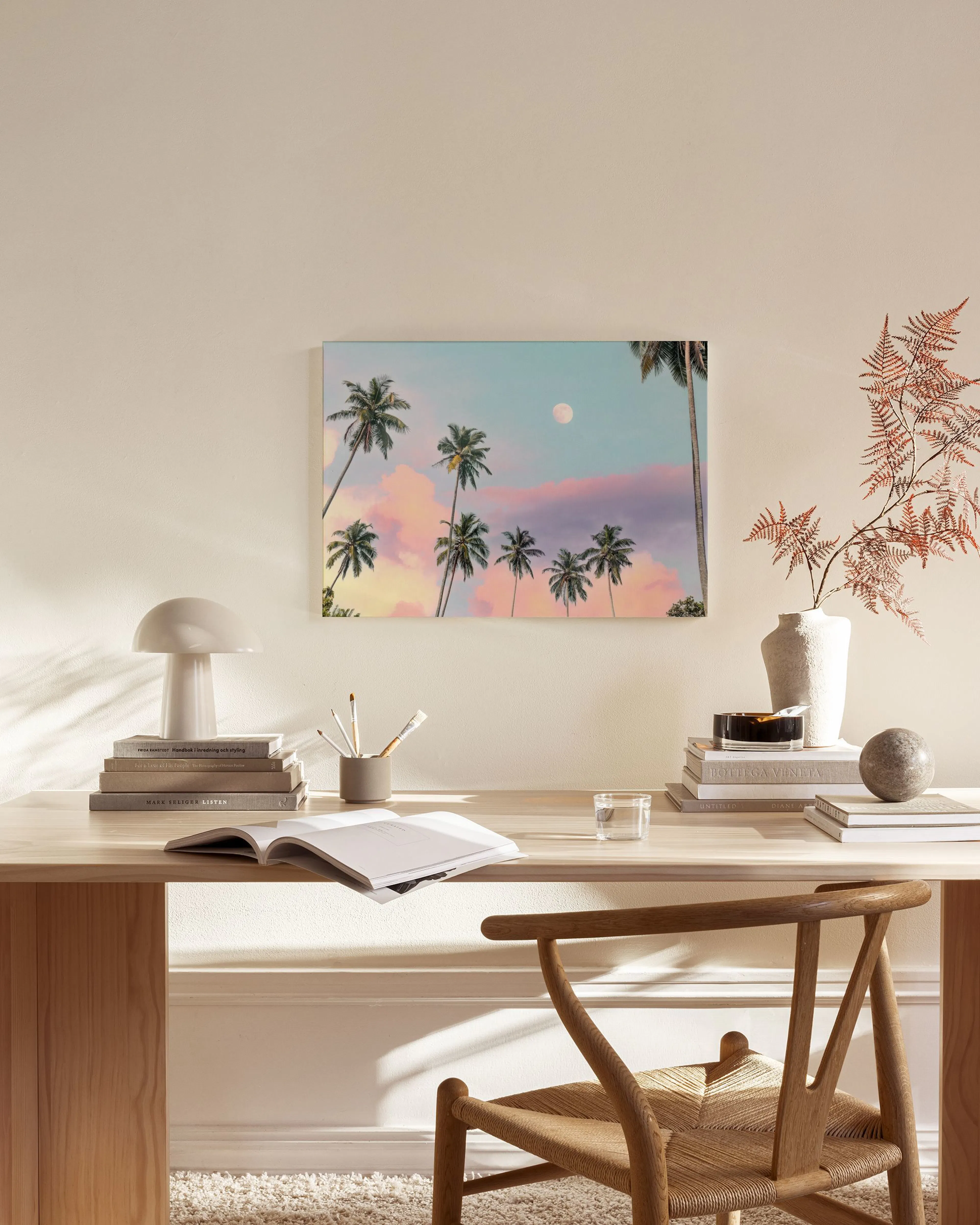 Lienzo de palmeras bajo una luna plateada y un cielo rosado y azul, colgado en una sala de estar moderna.