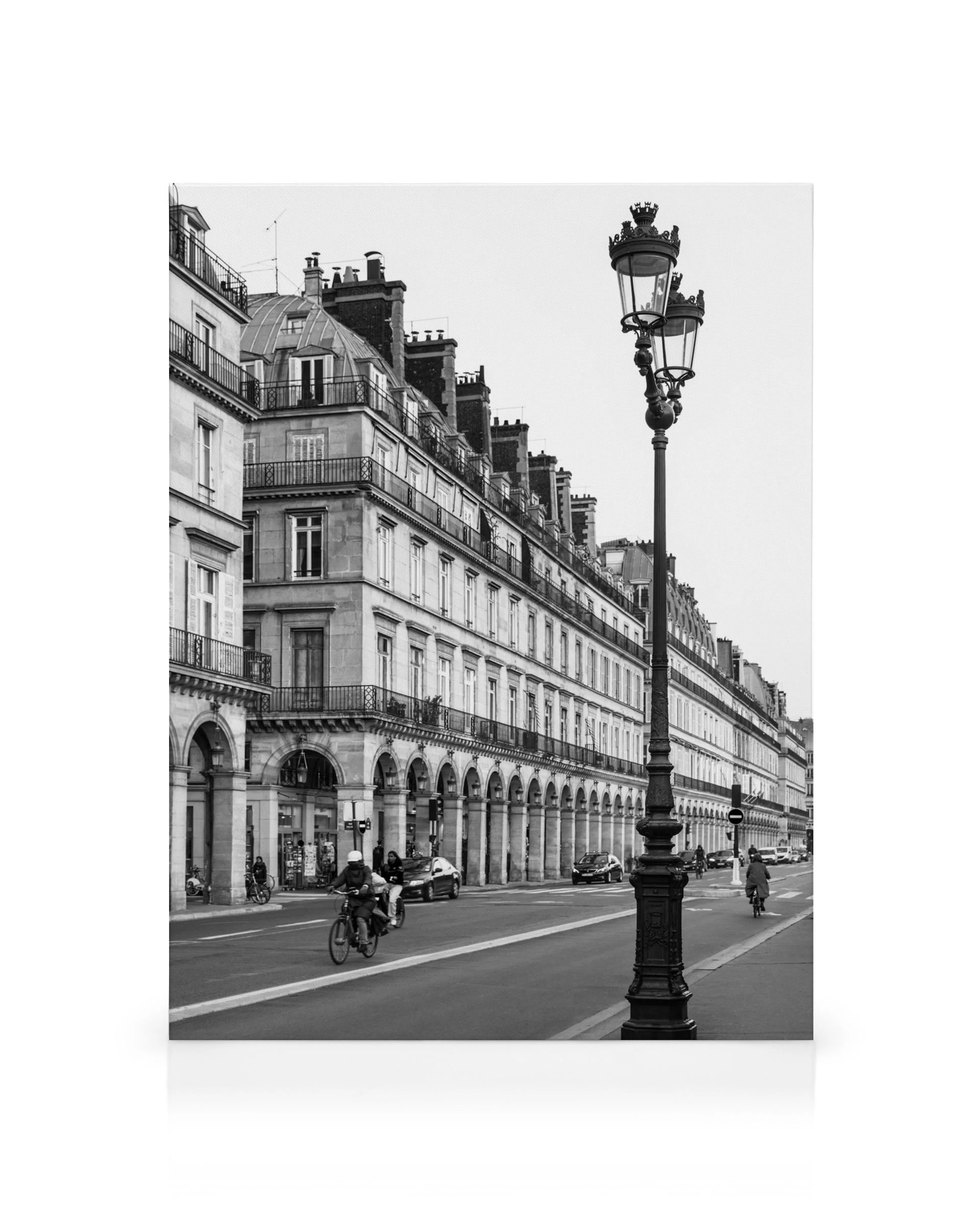 Schwarz-weißes Pariser Straßenbild mit Haussmann-Gebäuden, Arkaden, Laterne, Menschen und Fahrrädern.