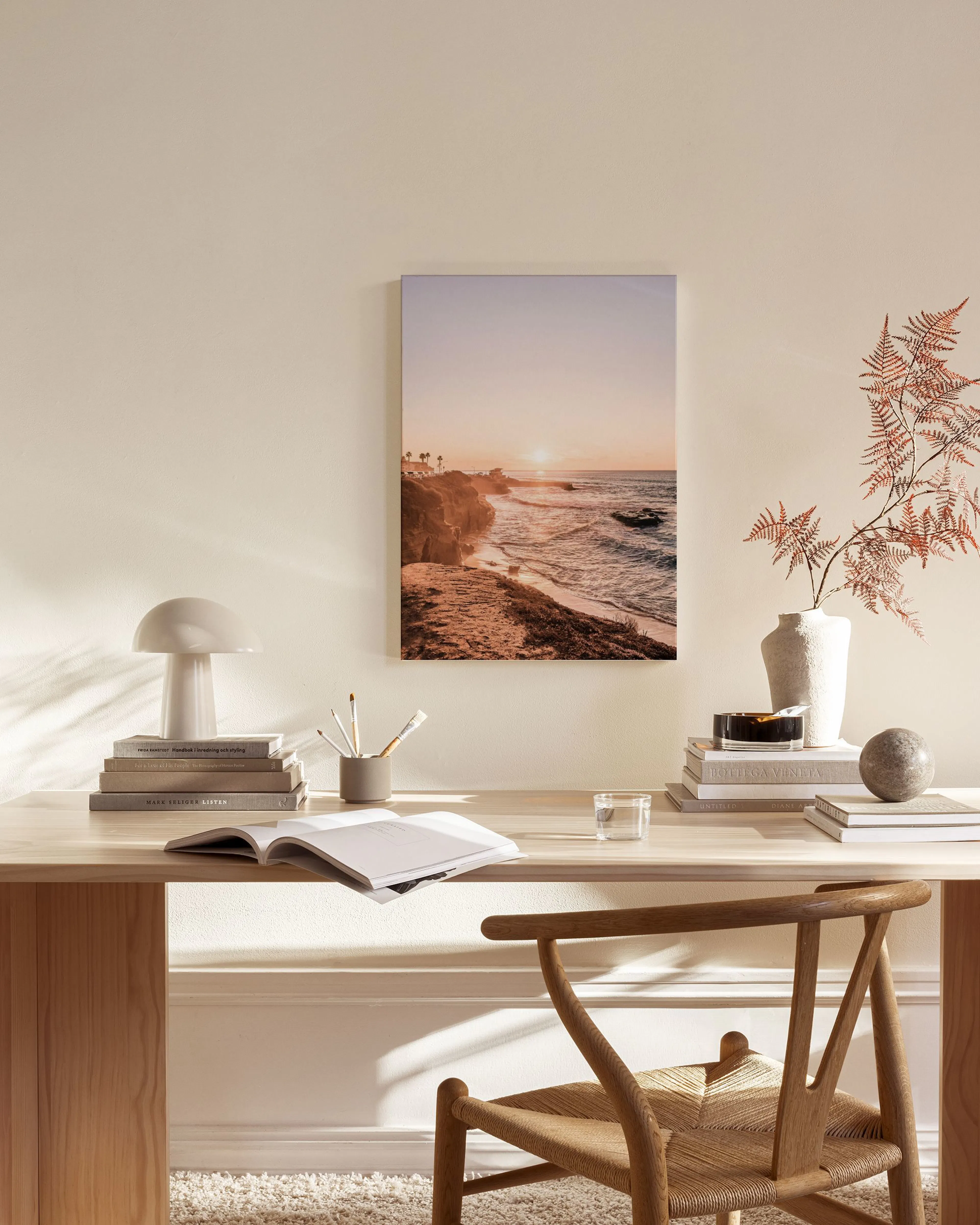 A canvas print of a golden sunset over a rocky coastline, hanging above a light wood console table in a minimalist living room.