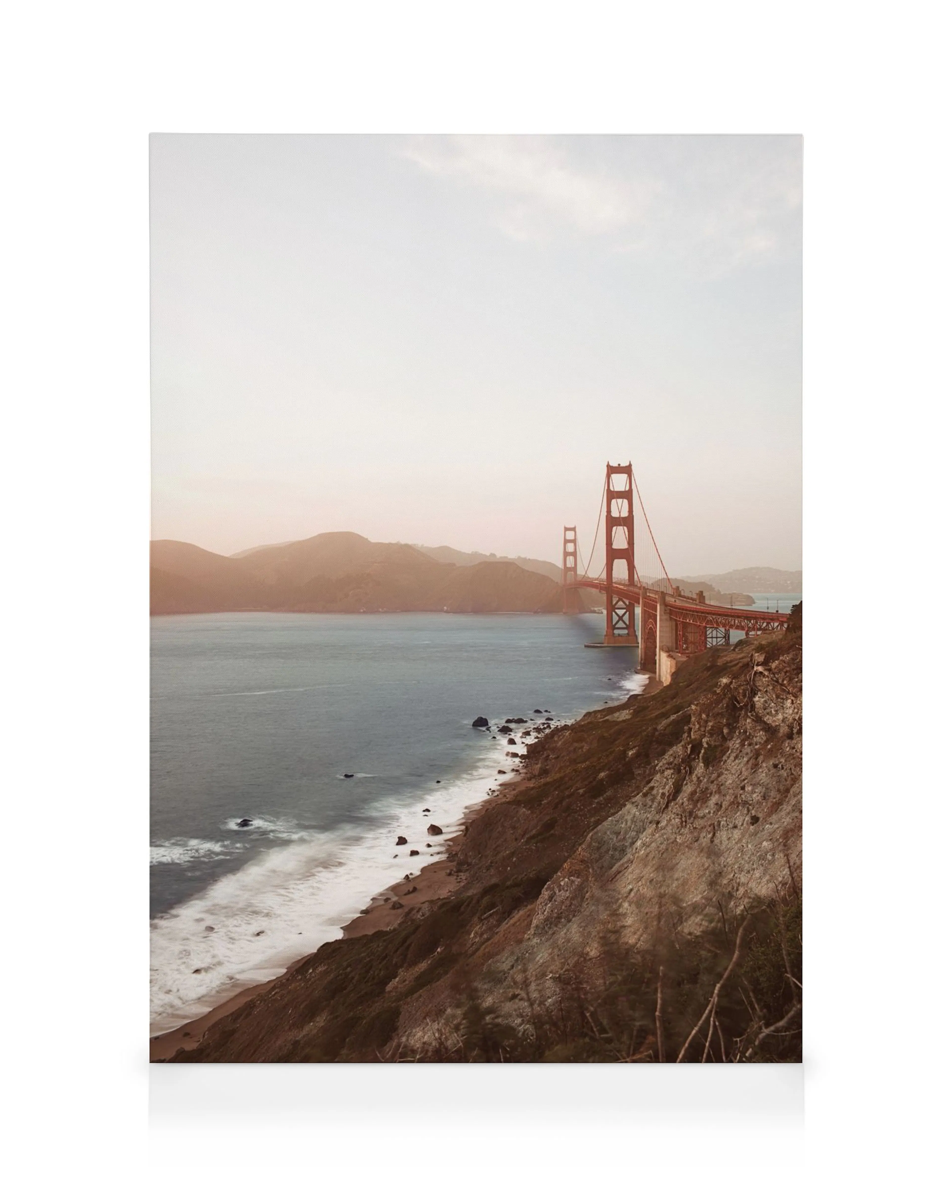 Leinwandbild der Golden Gate Bridge in der Abenddämmerung, mit sanften Wellen am felsigen Ufer und Hügeln im Hintergrund.