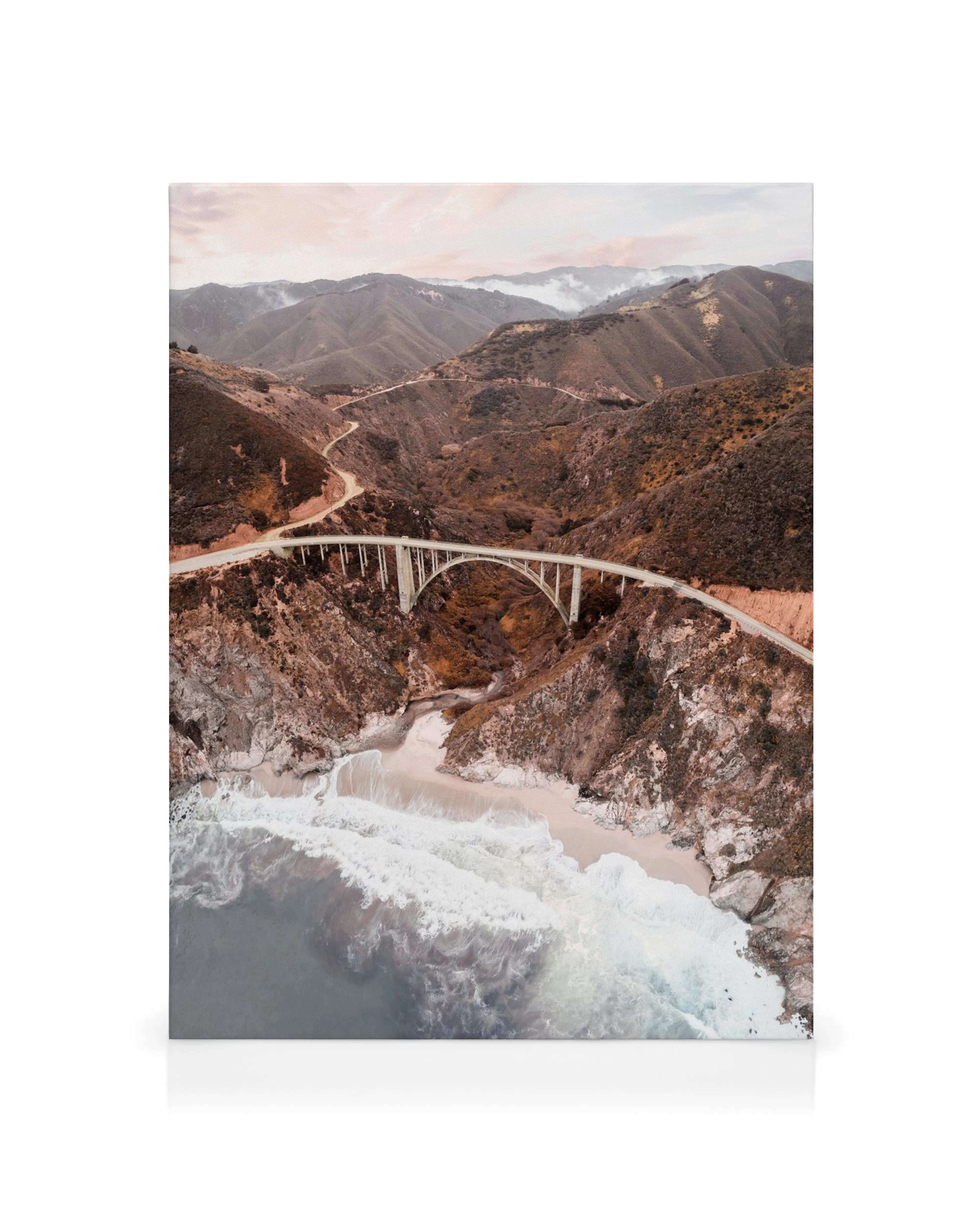 Lienzo del puente Bixby Creek sobre un cañón, con río y carreteras serpenteantes en montañas rosadas y marrones.
