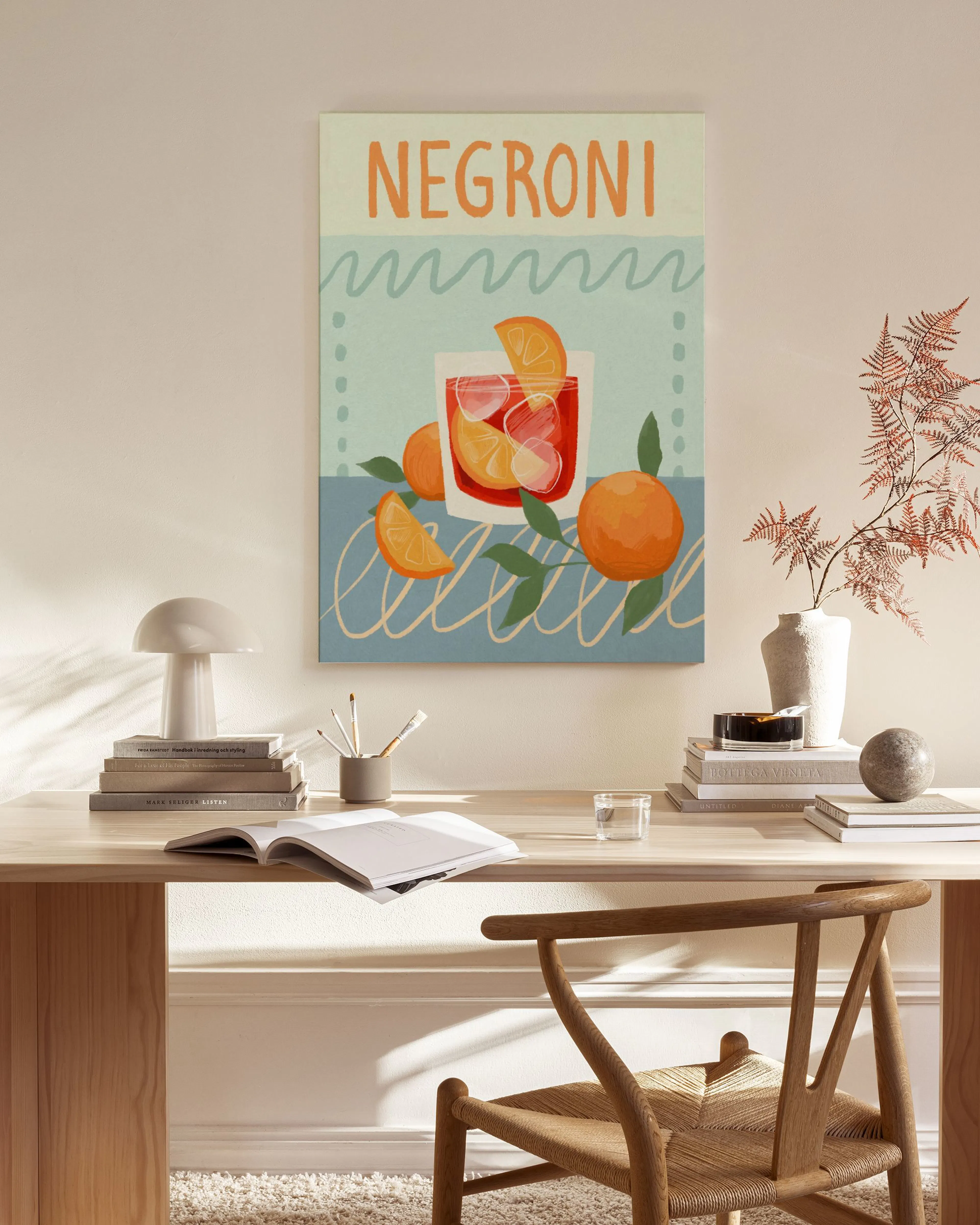 A Negroni cocktail canvas print with oranges and blue waves, hanging in a bright, modern living room above a wooden console.