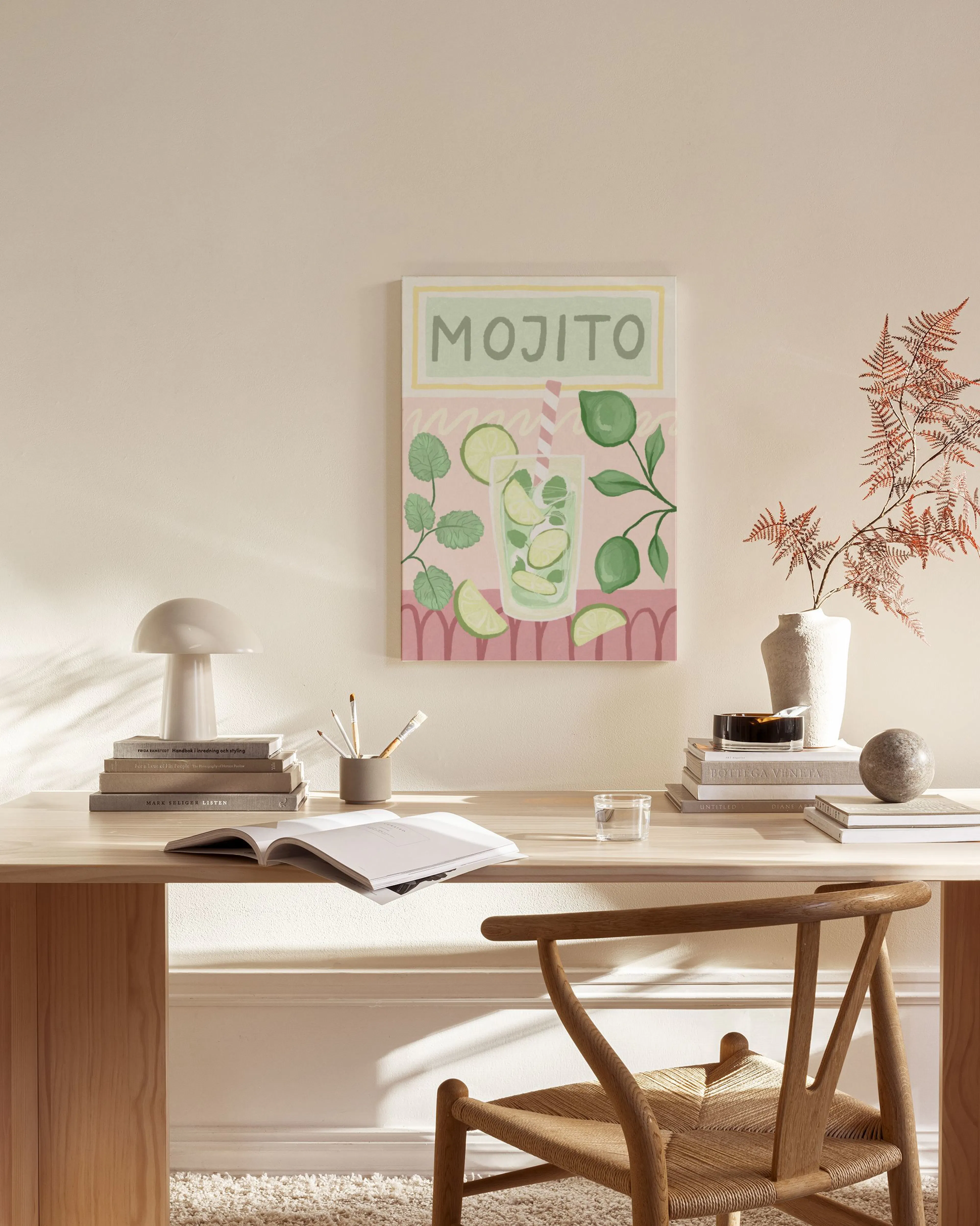 Lærred med mojito-motiv i lysegrønne og lyserøde nuancer, hængende i en stue over en træbænk.