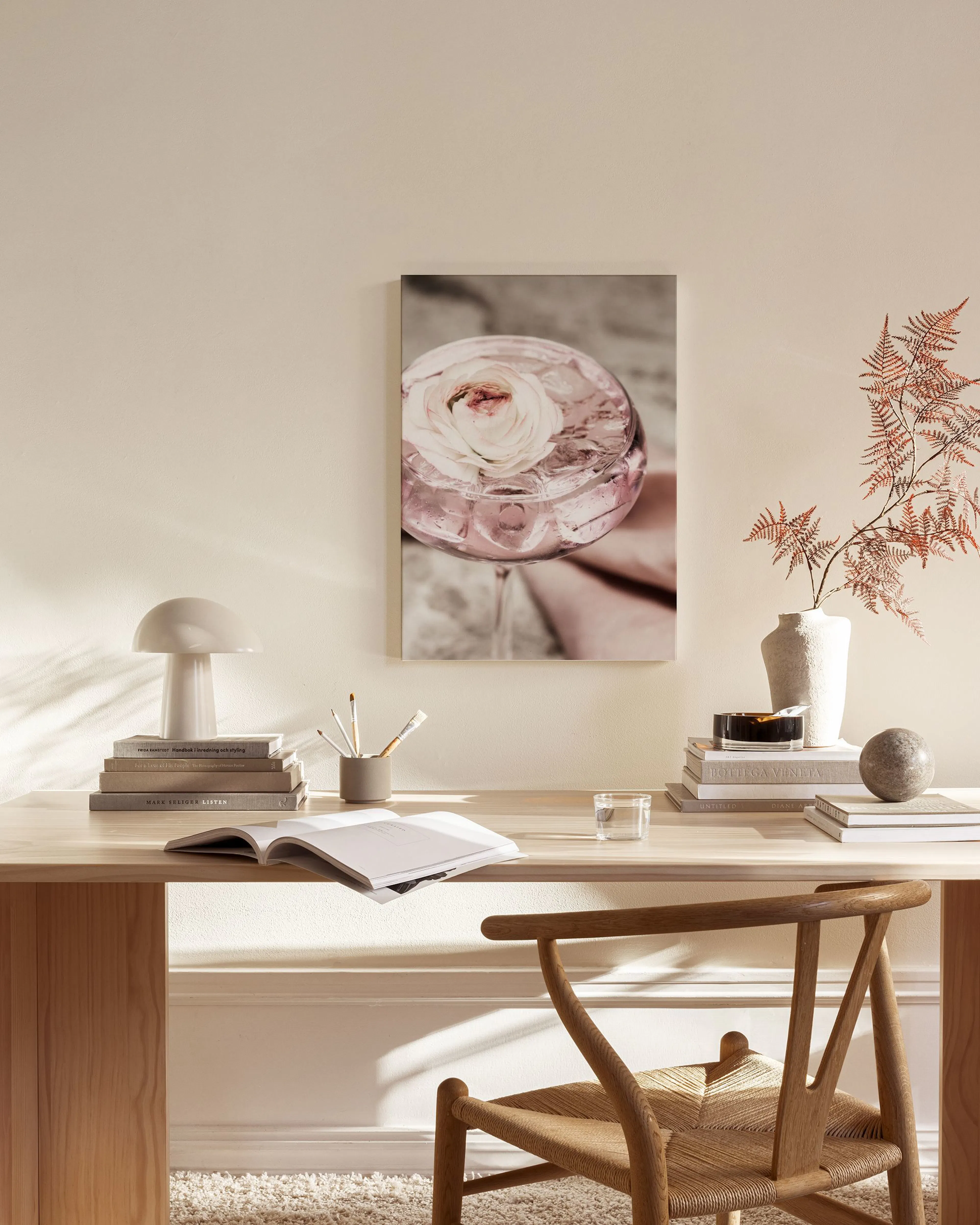 A canvas print of a pink cocktail with a white flower and ice, hanging in a minimalist living room above a wooden console.