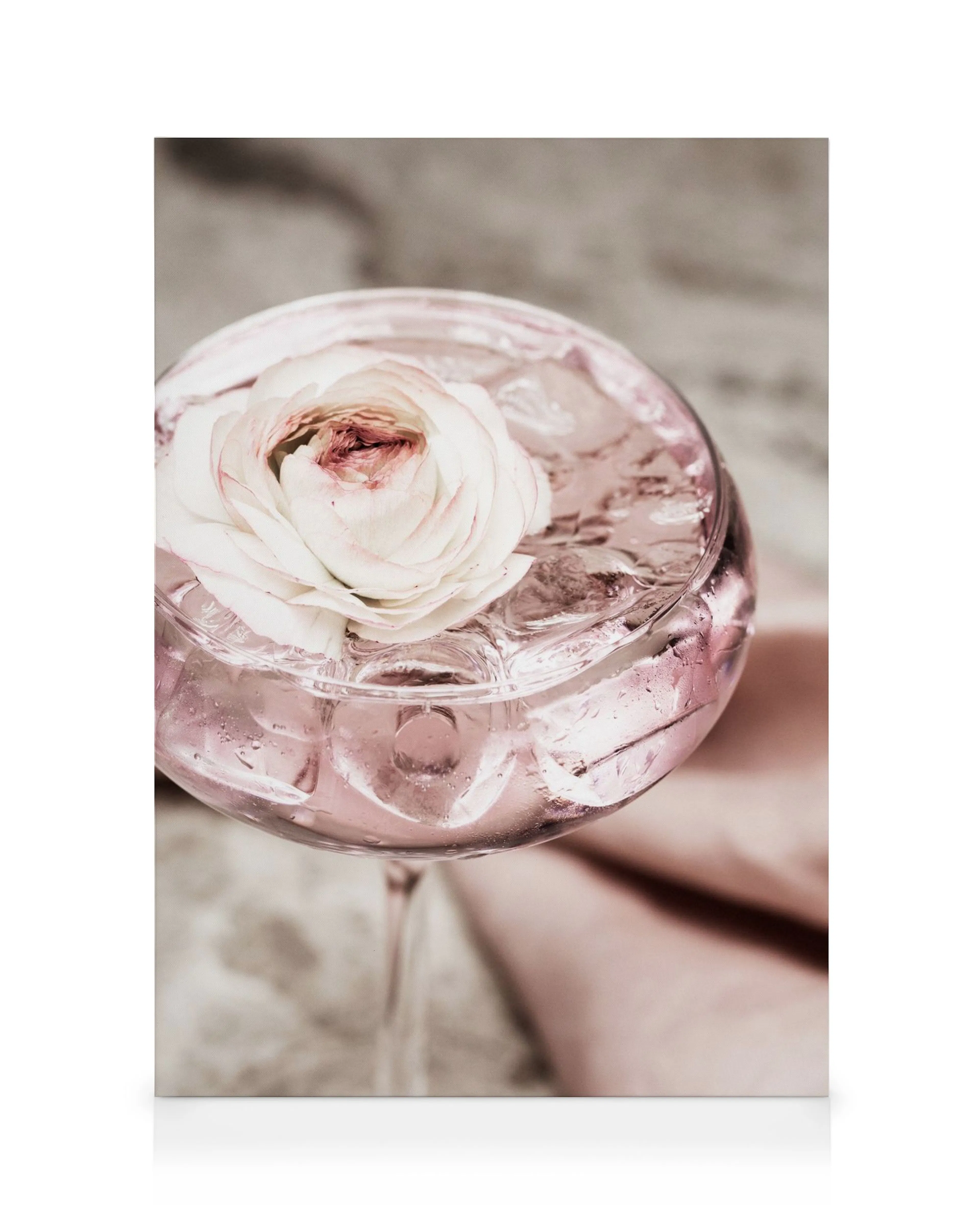 Ett glas med rosa cocktail och isbitar, toppat med en vit och rosa blomma.