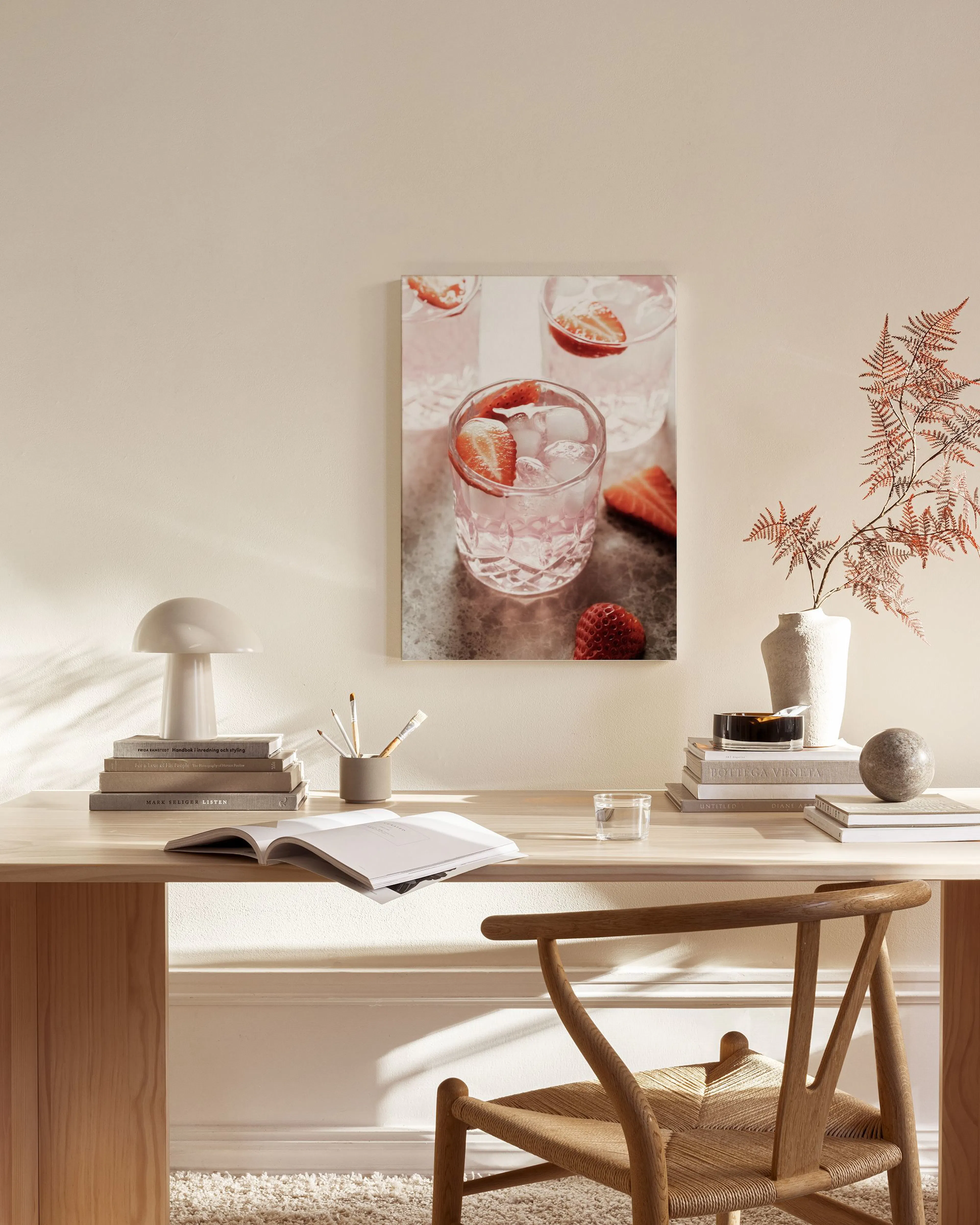 Leinwandbild mit rosa Getränken, Eiswürfeln und Erdbeeren, hängend über einem Sideboard in einem hellen Wohnzimmer.