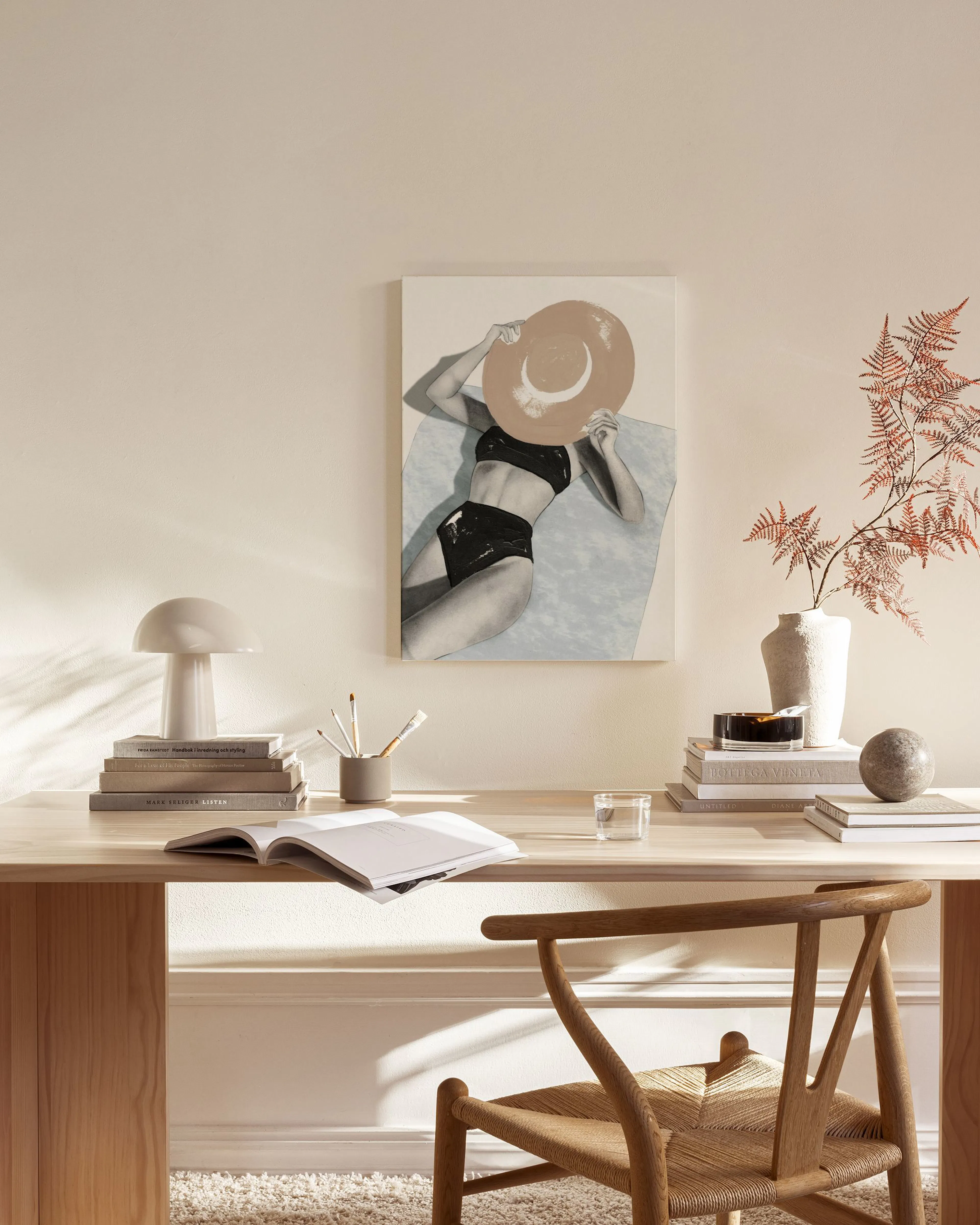A canvas print of a woman in a black bikini and sun hat, displayed in a minimalist living room above a wooden console table.