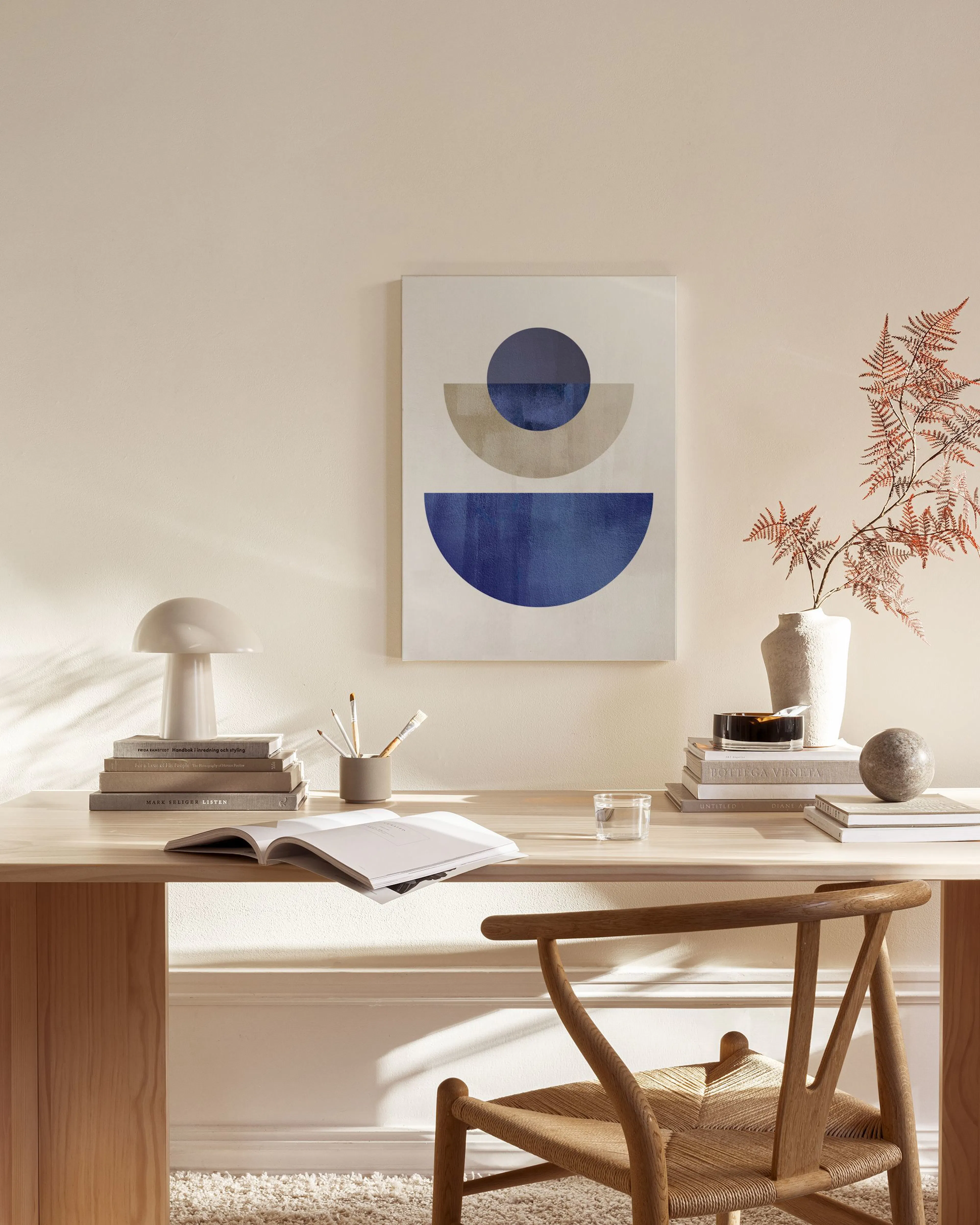 Tela decorativa com formas geométricas em tons de azul e bege, pendurada numa sala de estar minimalista.