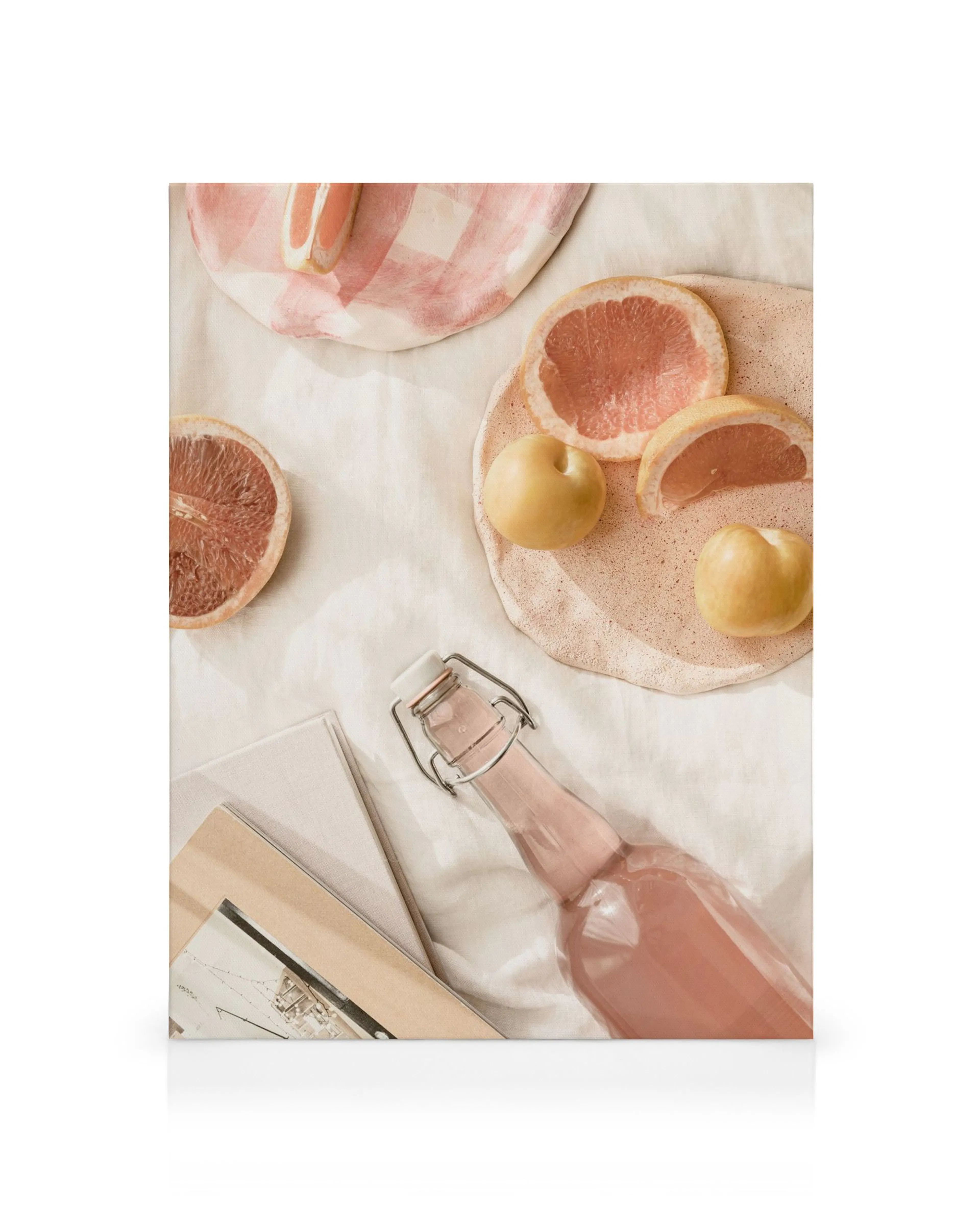 Canvas print with pink patterned plates, grapefruit, lemons, and a glass bottle on white cloth.