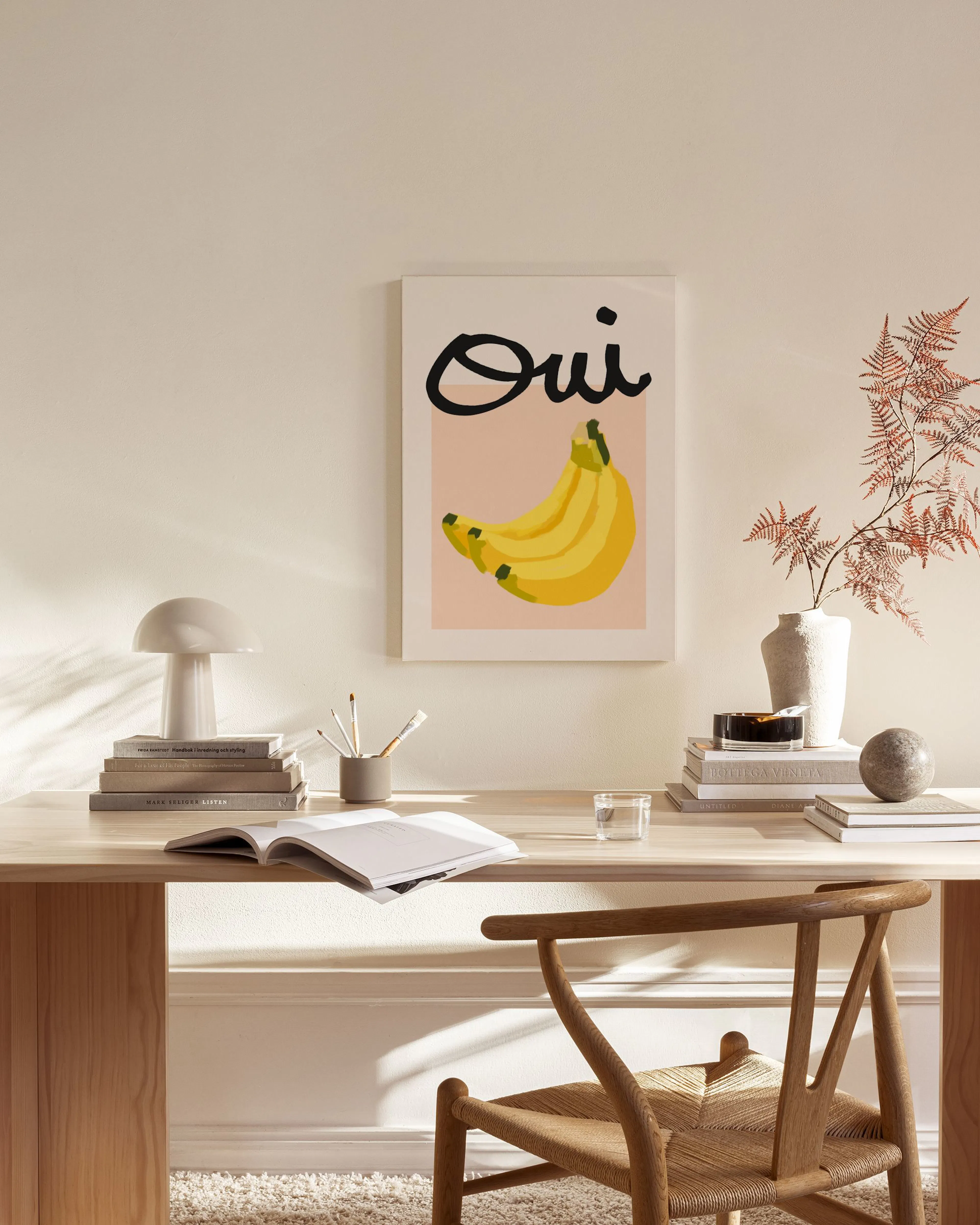 Canvas met zwarte Oui tekst en gele bananen op een roze achtergrond, hangend in een lichte woonkamer.