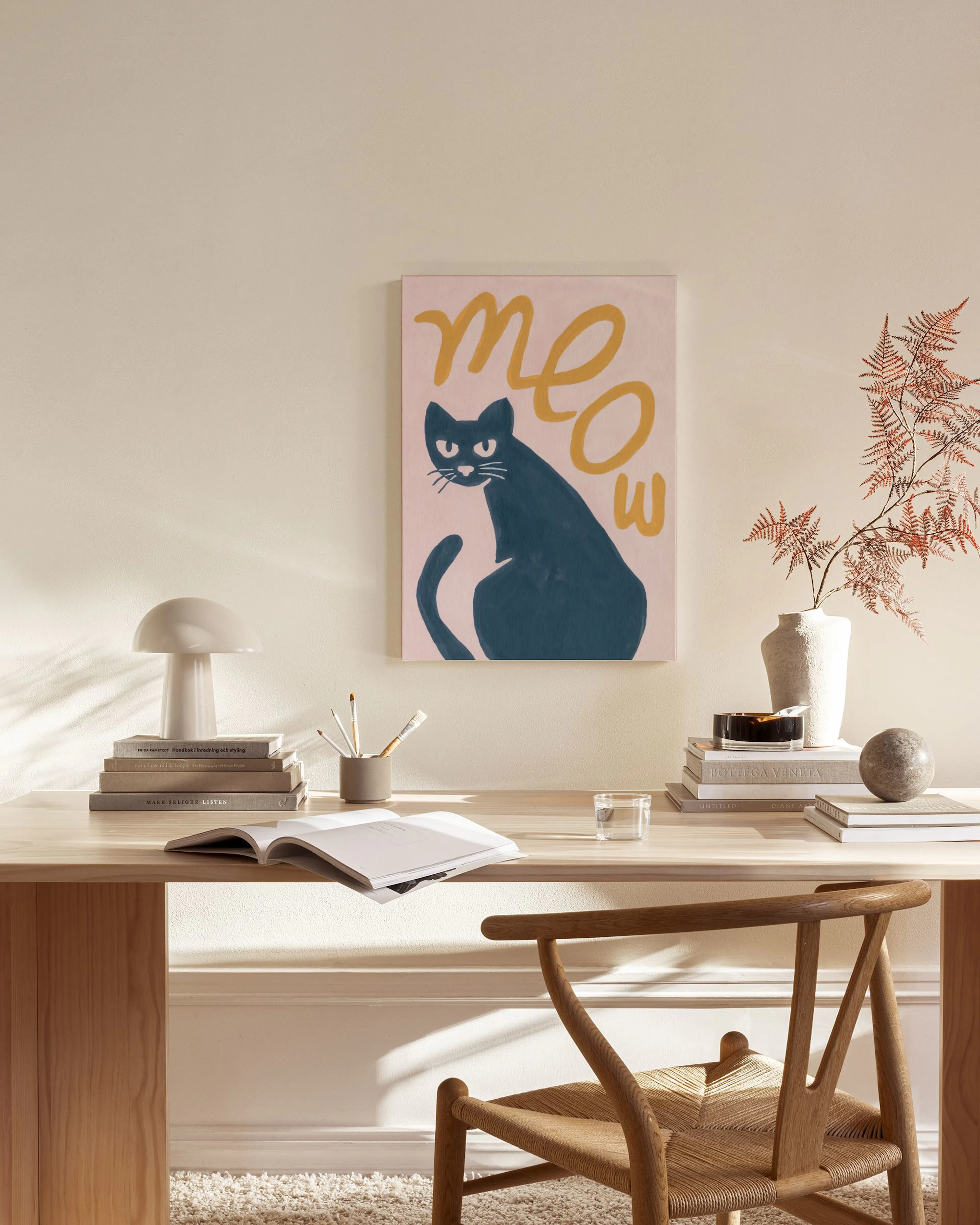 Lerretsbilde med en blå katt og meow i gult, henger over et lavt bord i en lys stue.