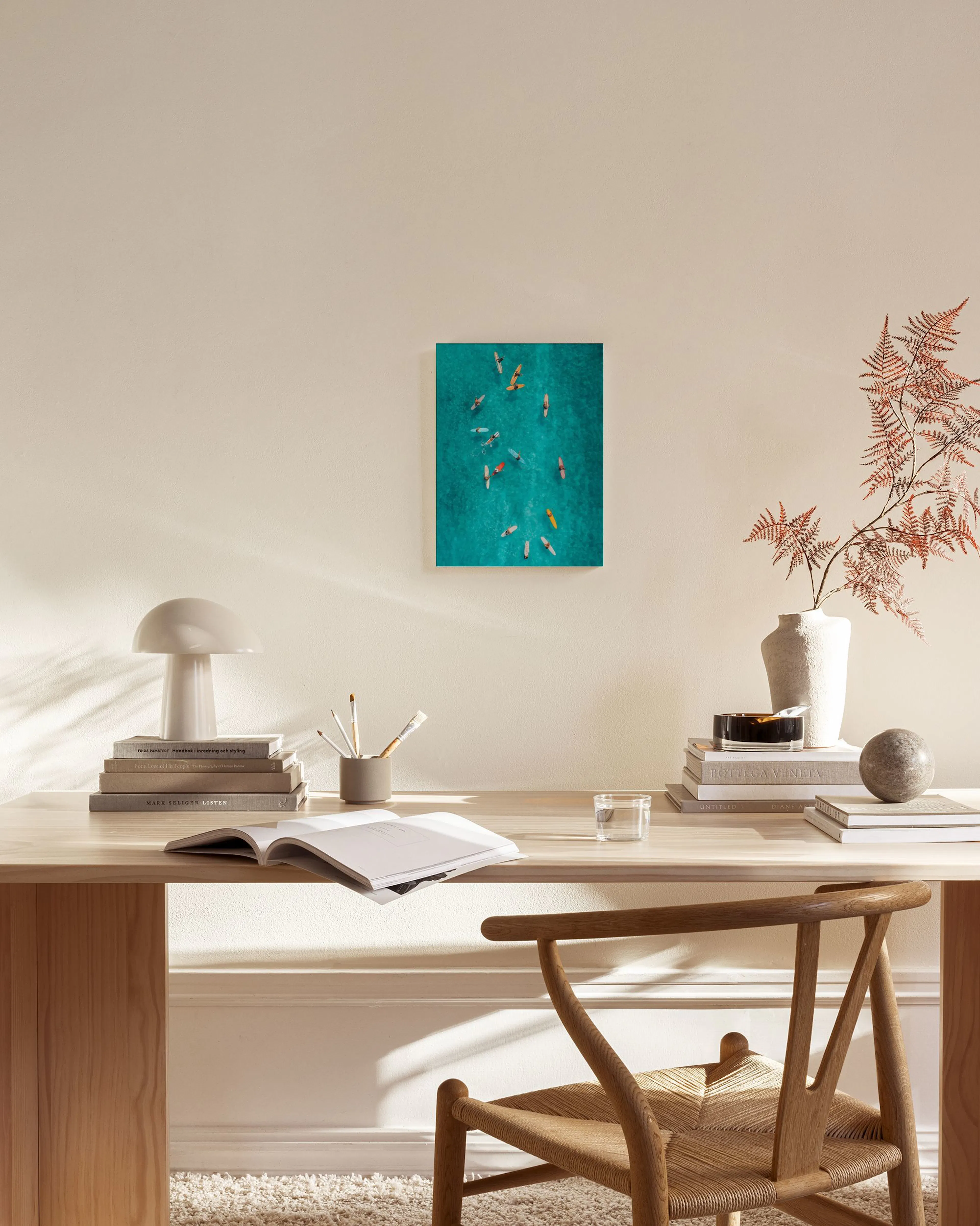Aerial photo of surfers on turquoise water, hanging above a console table in a bright, modern living room.