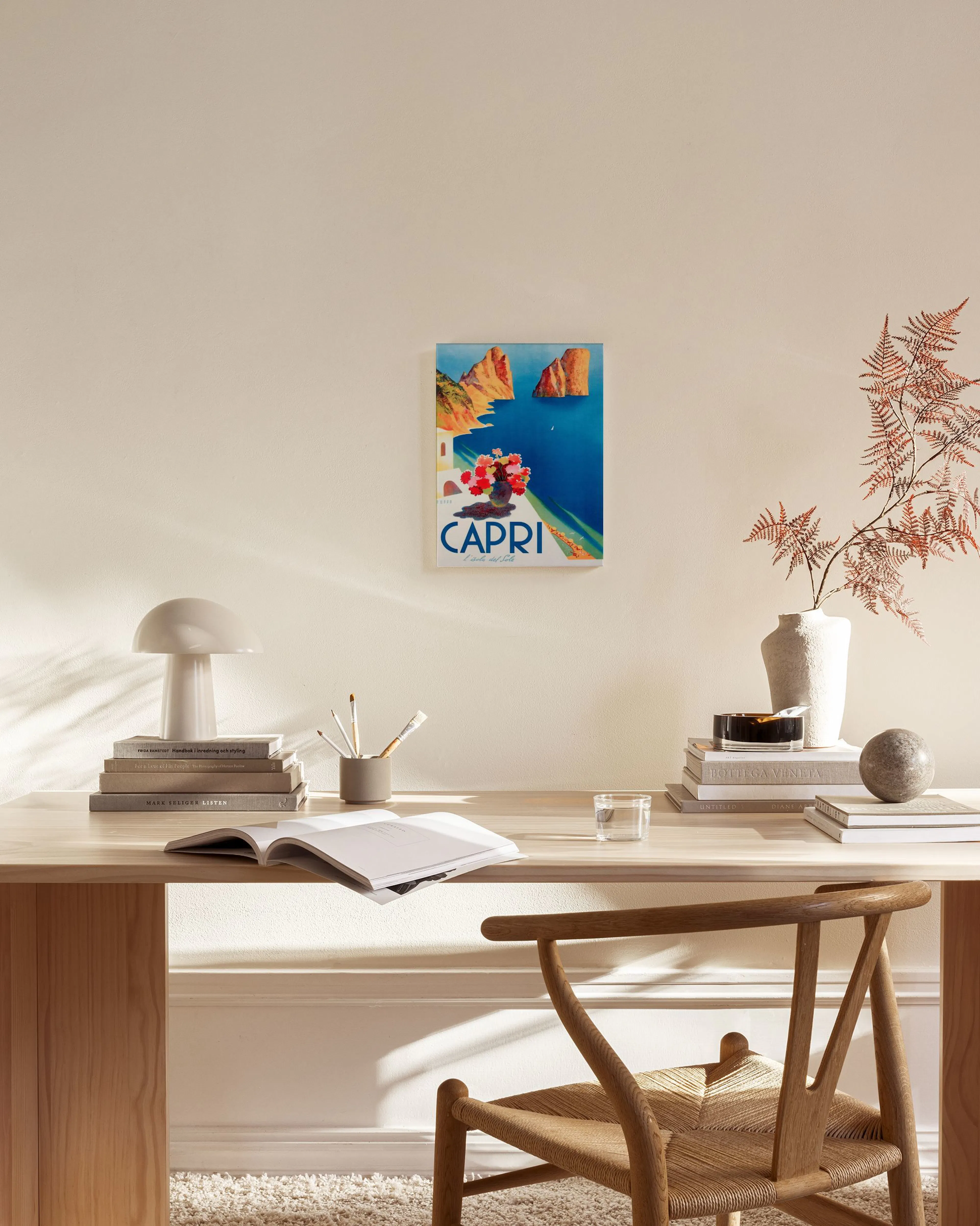 Leinwandbild mit Capri-Motiv über einem Sideboard, das Meer, Felsen und Blumen zeigt, in einem modernen Wohnzimmer.