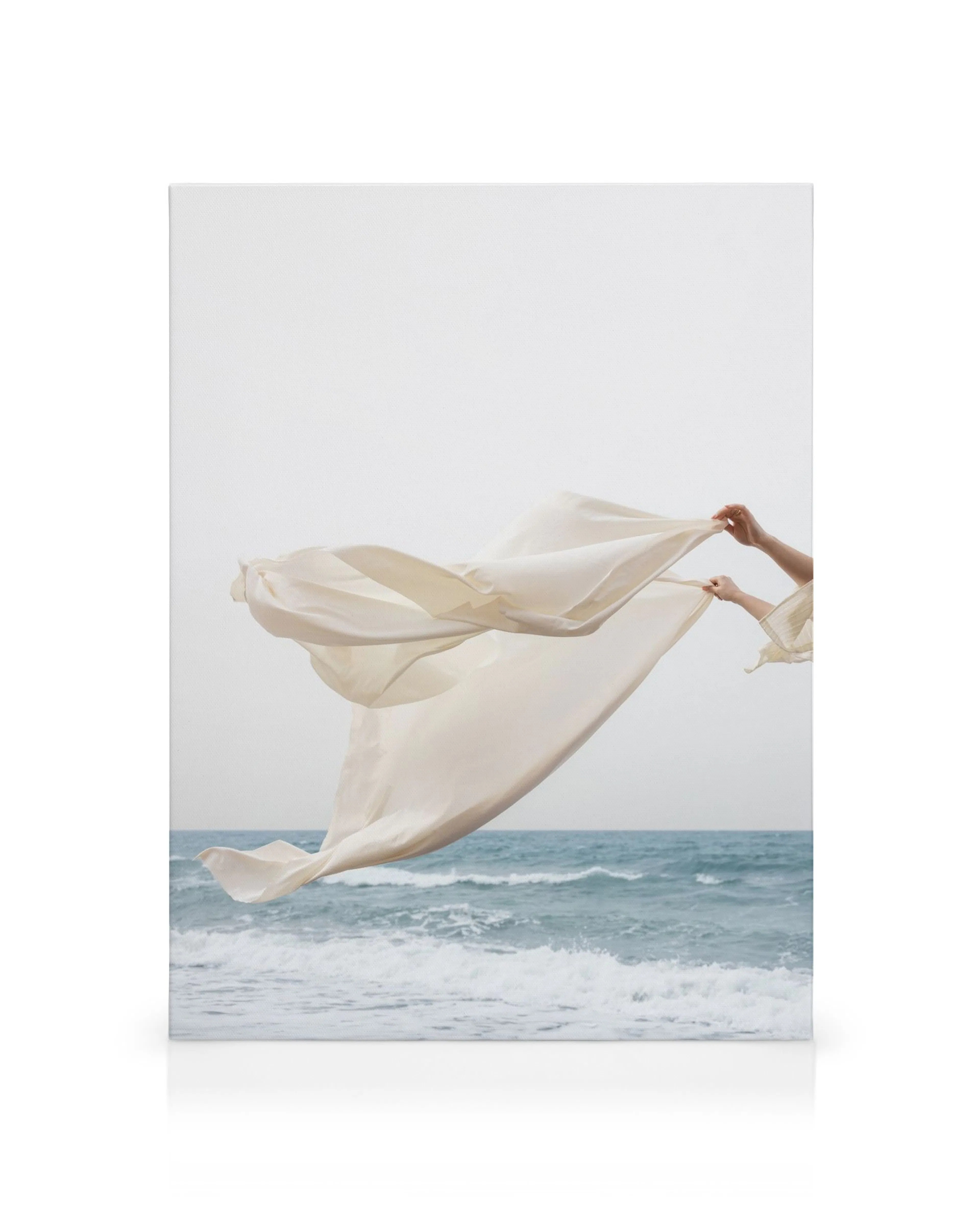 Hands holding a white fabric flowing in the wind above a blue sea with waves, canvas print.