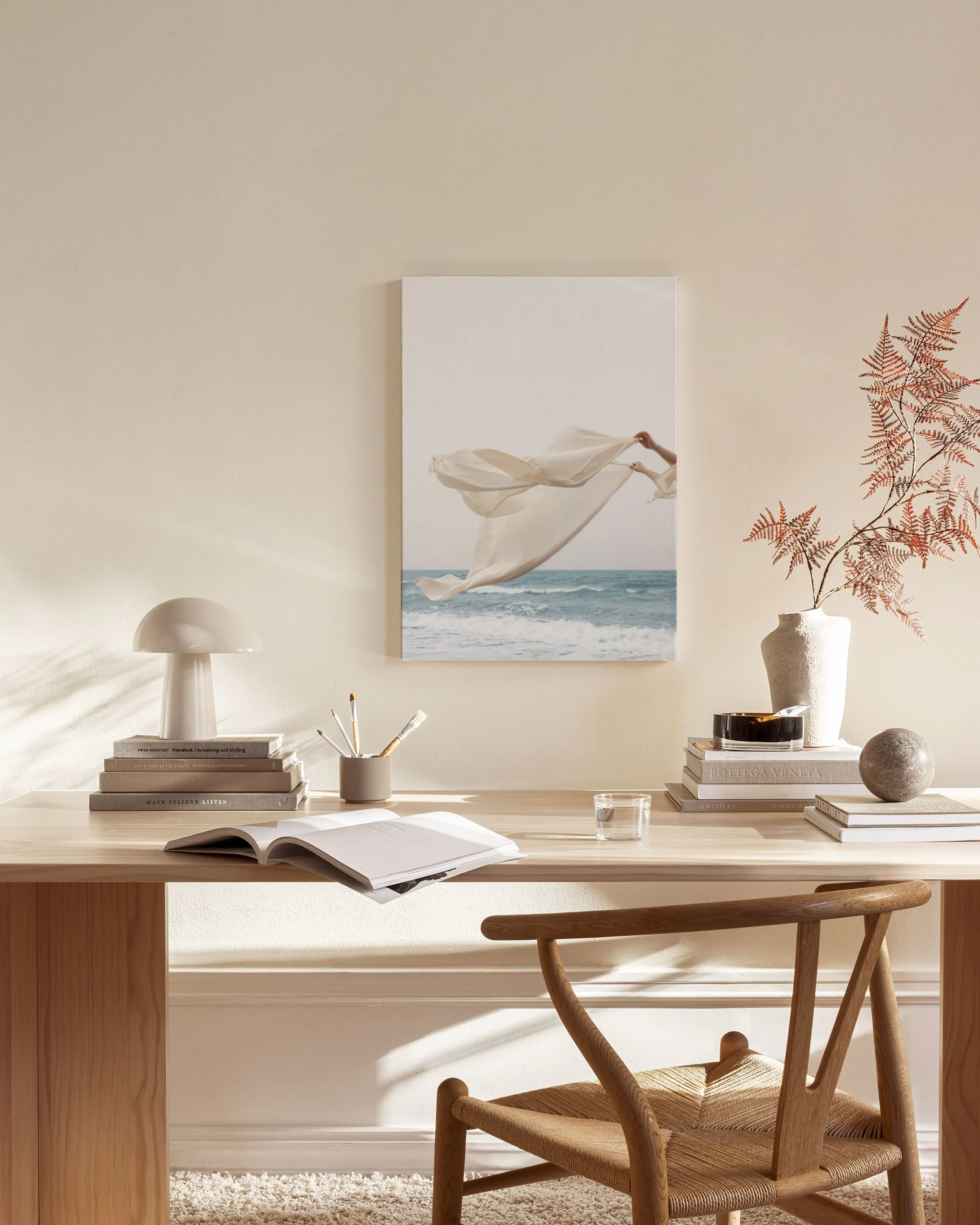 A canvas print of a hand holding flowing white fabric above blue ocean waves, displayed in a bright, modern living room.
