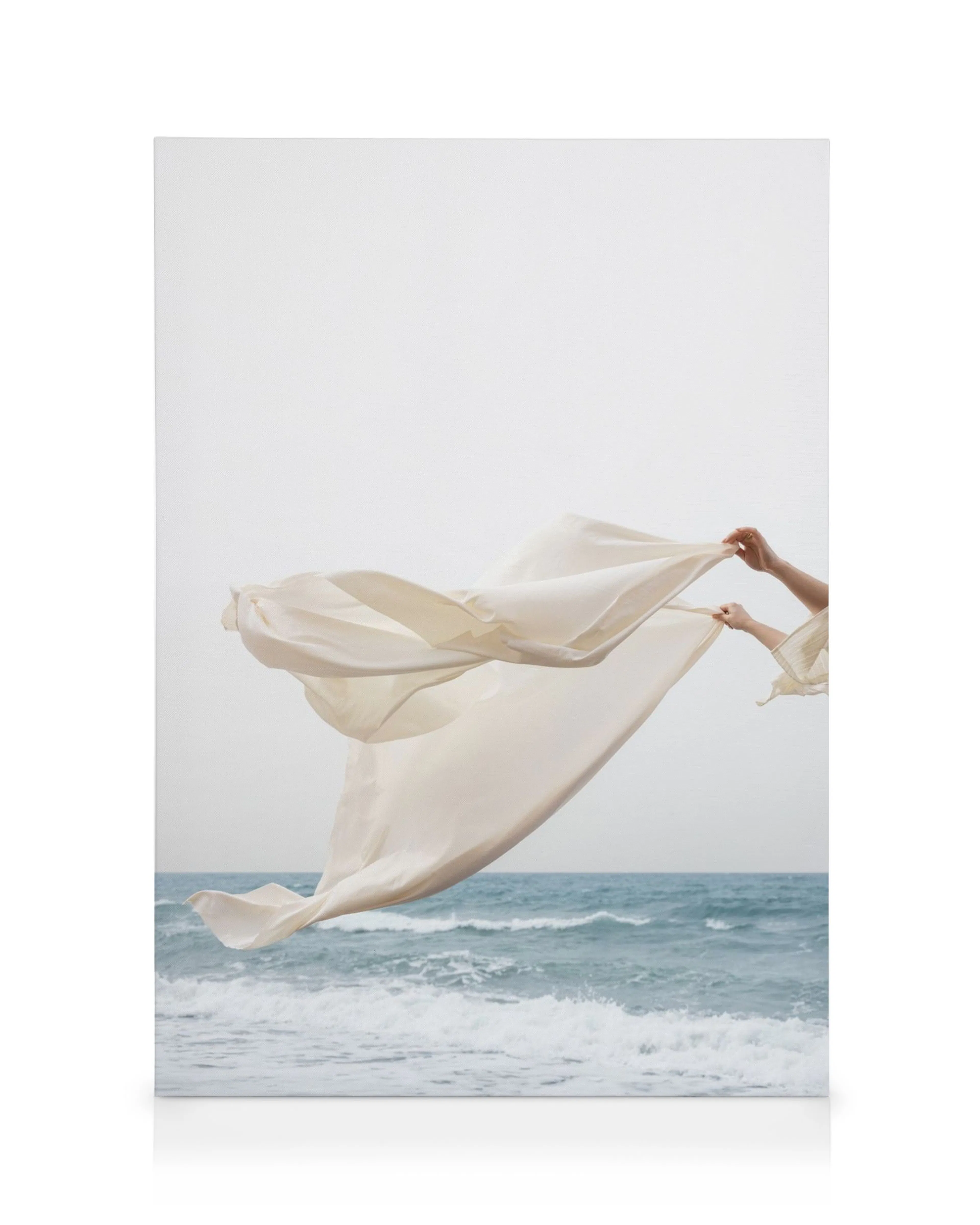 Canvas print of beige fabric flowing above blue and white ocean waves, held by hands.