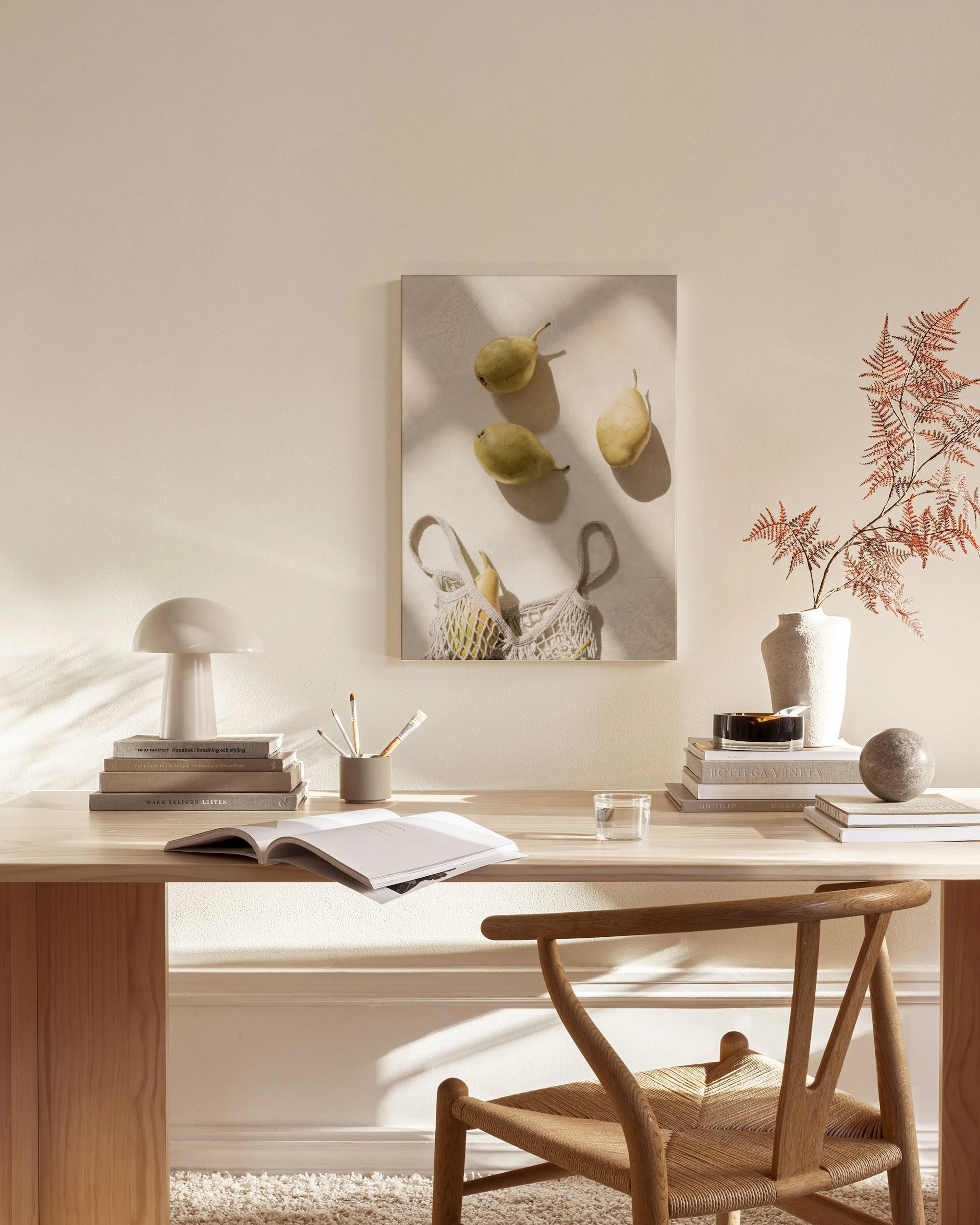 A canvas print of three pears and a mesh bag with fruit, hanging on a cream wall above a wooden console table in a minimalist li