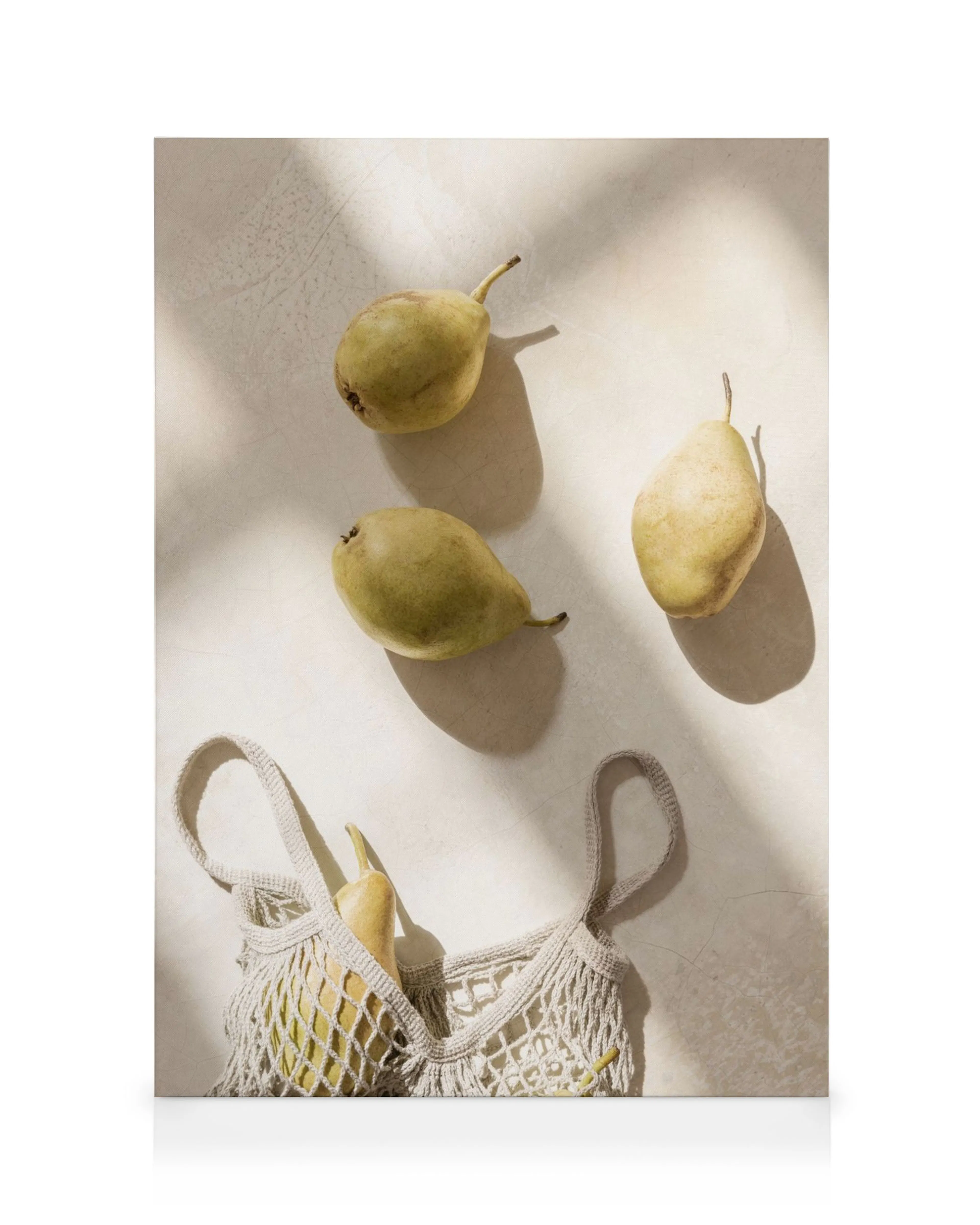 Three green pears on a textured surface, one in a white mesh bag, bathed in sunlight. Kitchen fruit art.