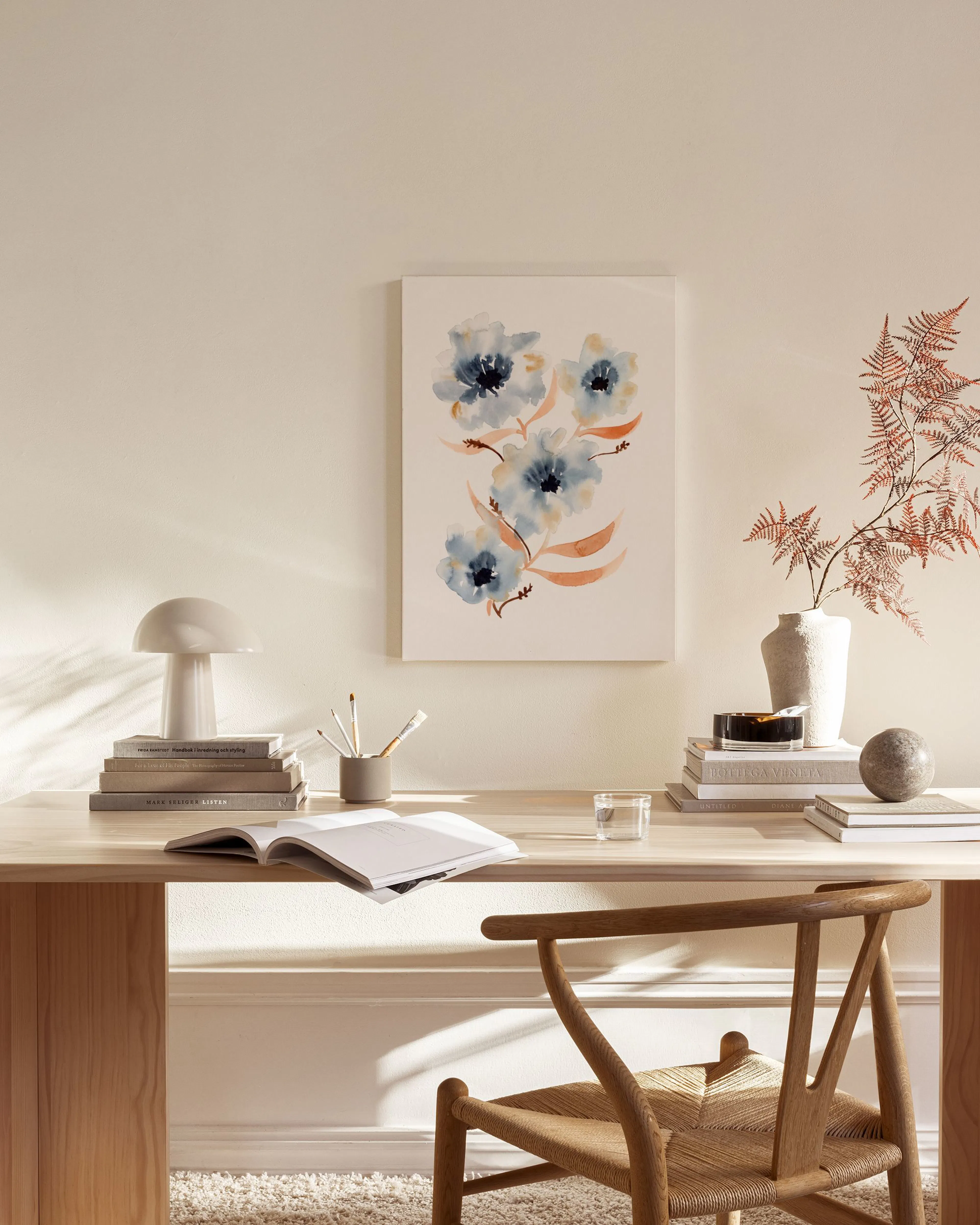 Stampa su tela con fiori acquerellati blu e foglie arancioni, appesa in un salotto moderno.