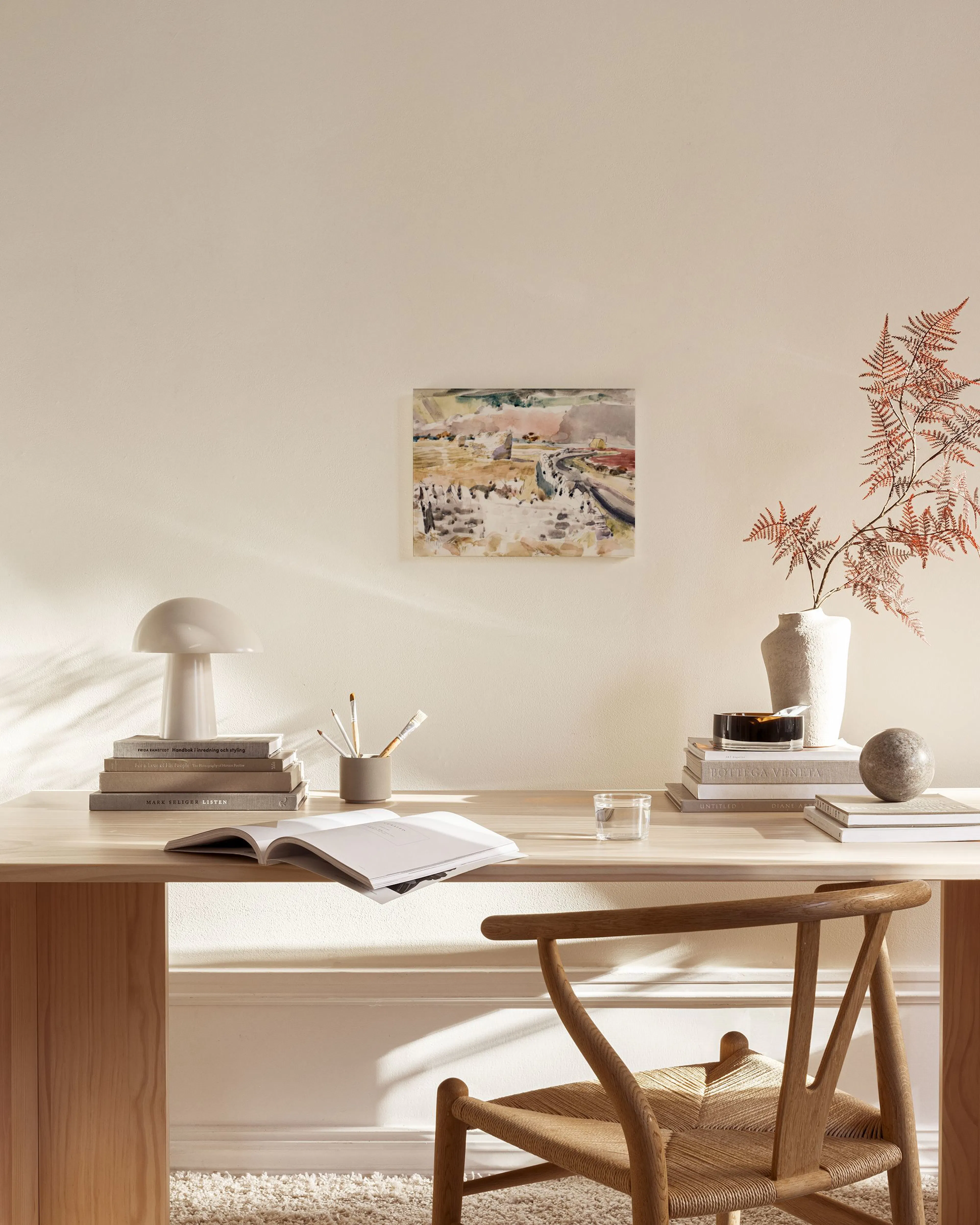 A watercolor landscape canvas print with earthy tones of brown, red, green and grey, displayed above a wooden console table in a
