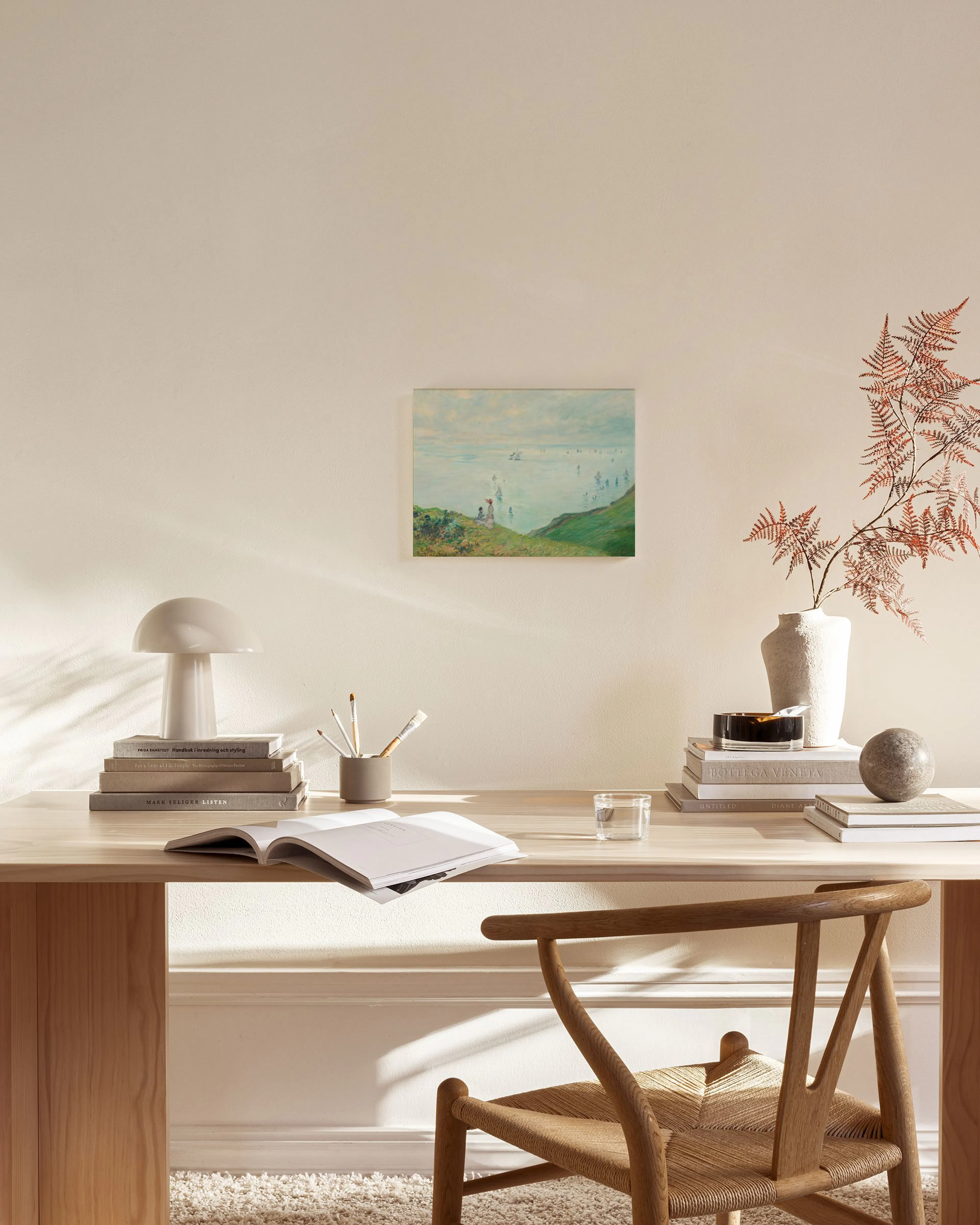 Impressionist painting of a blue sea with sailboats, green cliffs, and figures, hanging in a bright, minimalist living room.