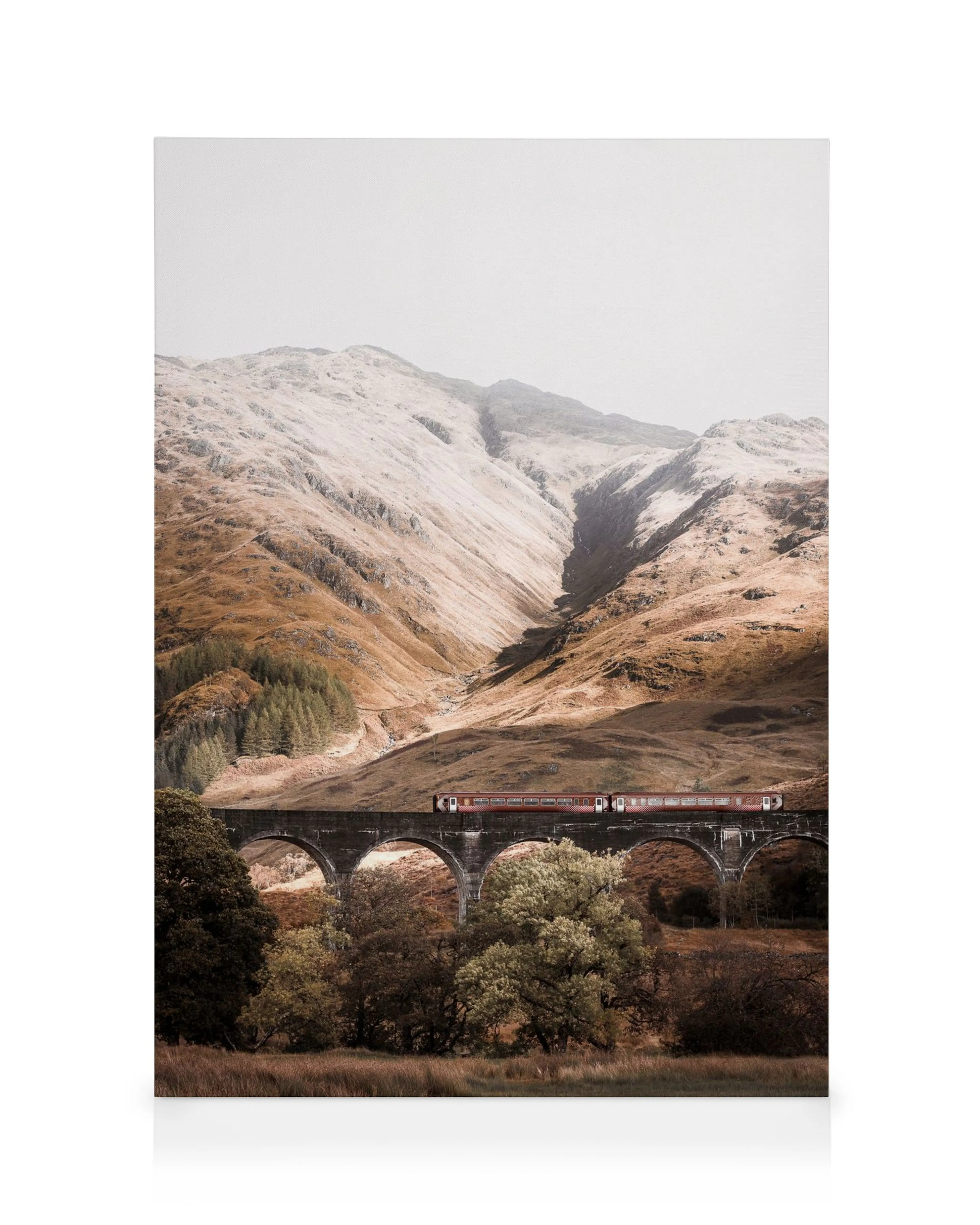 Red train crossing a historic stone viaduct over a valley, with rolling hills and mountains in the background.