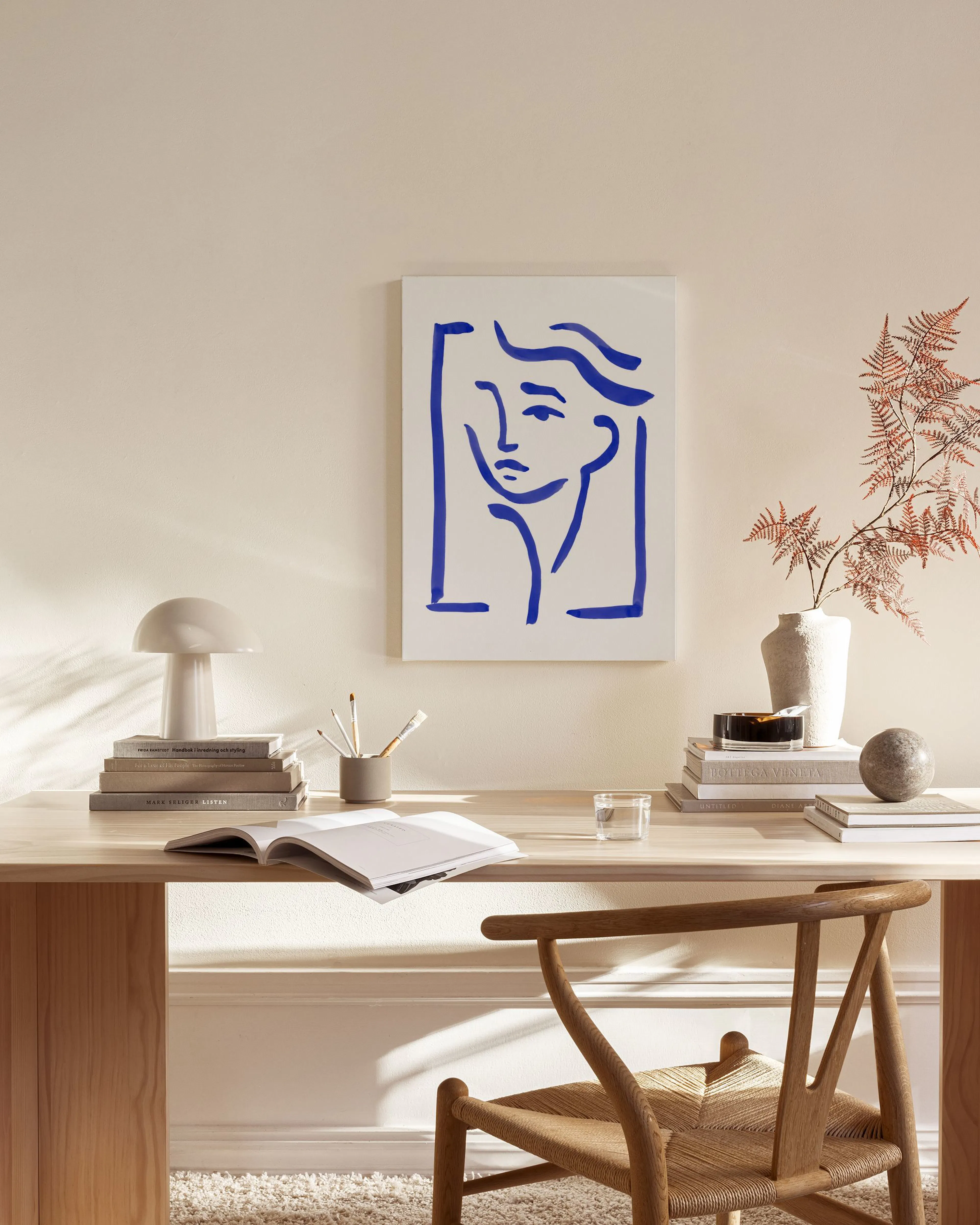 Leinwandbild mit abstraktem blauem Gesicht, das in einem hellen Wohnzimmer über einem Sideboard hängt.