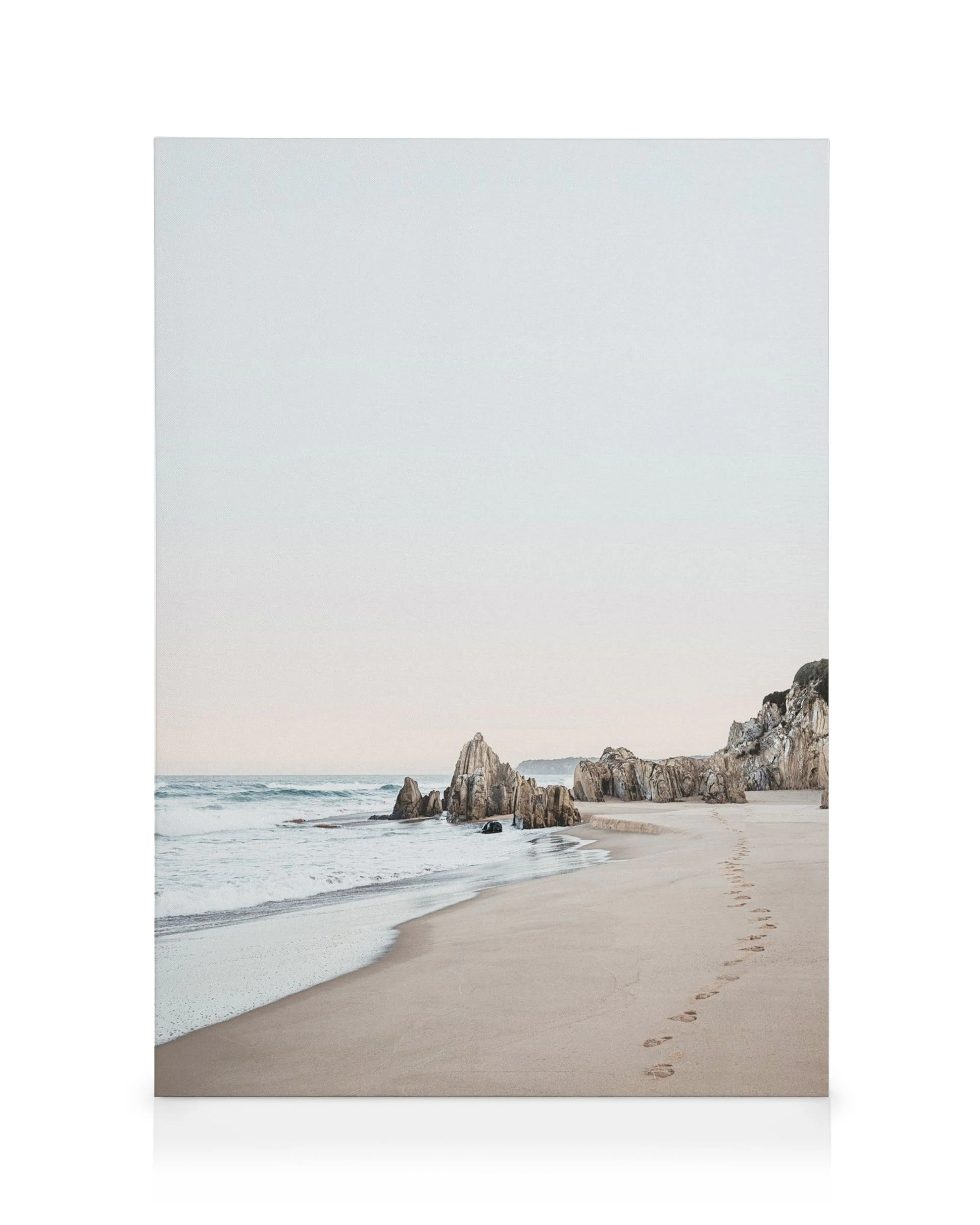 Toile de plage avec empreintes de pas dans le sable menant à des rochers et à la mer, couleurs bleues, brunes et beiges