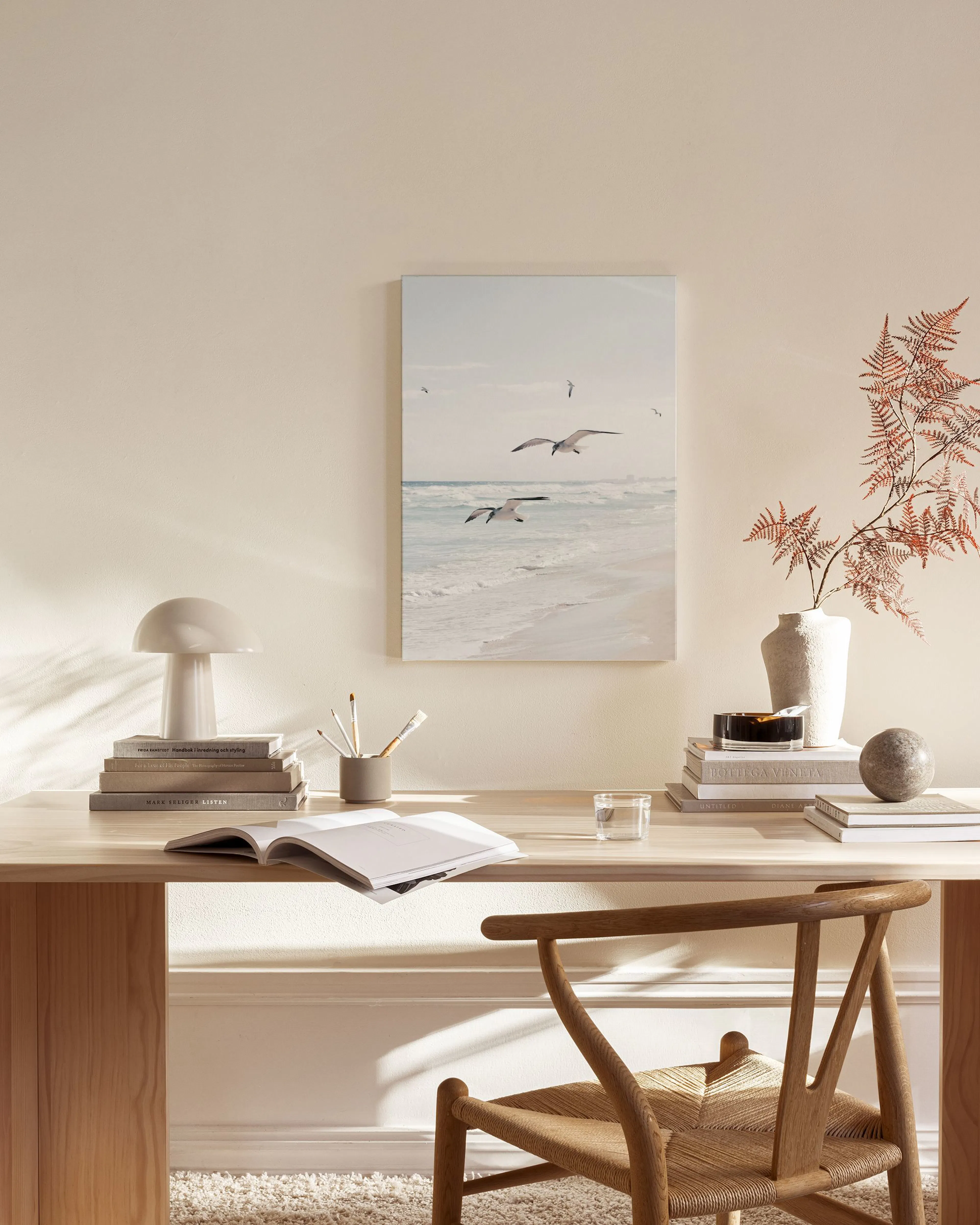 Coastal canvas print of seagulls flying over a sandy beach and ocean waves, hanging in a light-filled living room.