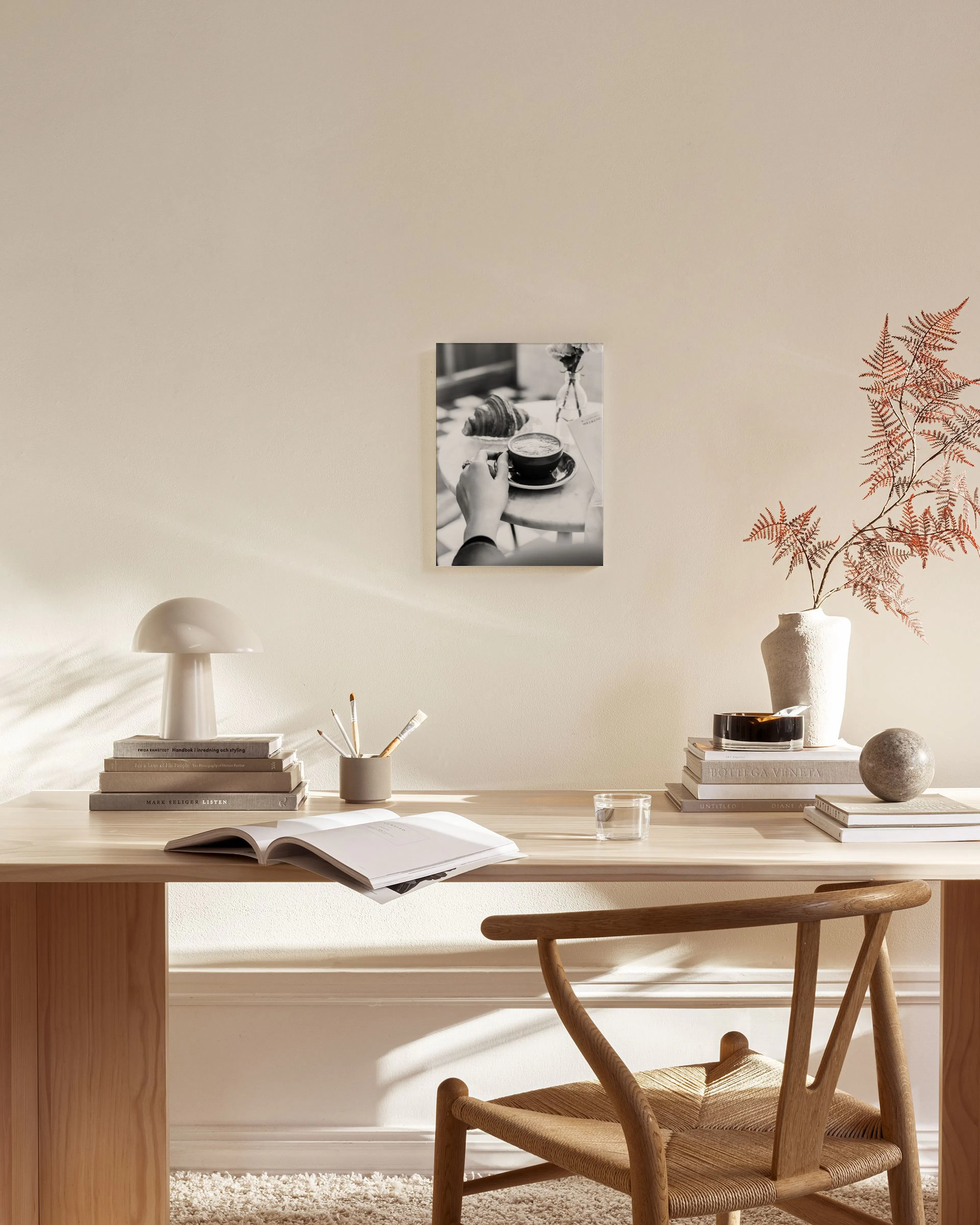 Zwart-wit canvas van een hand die een kop koffie vasthoudt met een croissant, hangend in een moderne woonkamer.