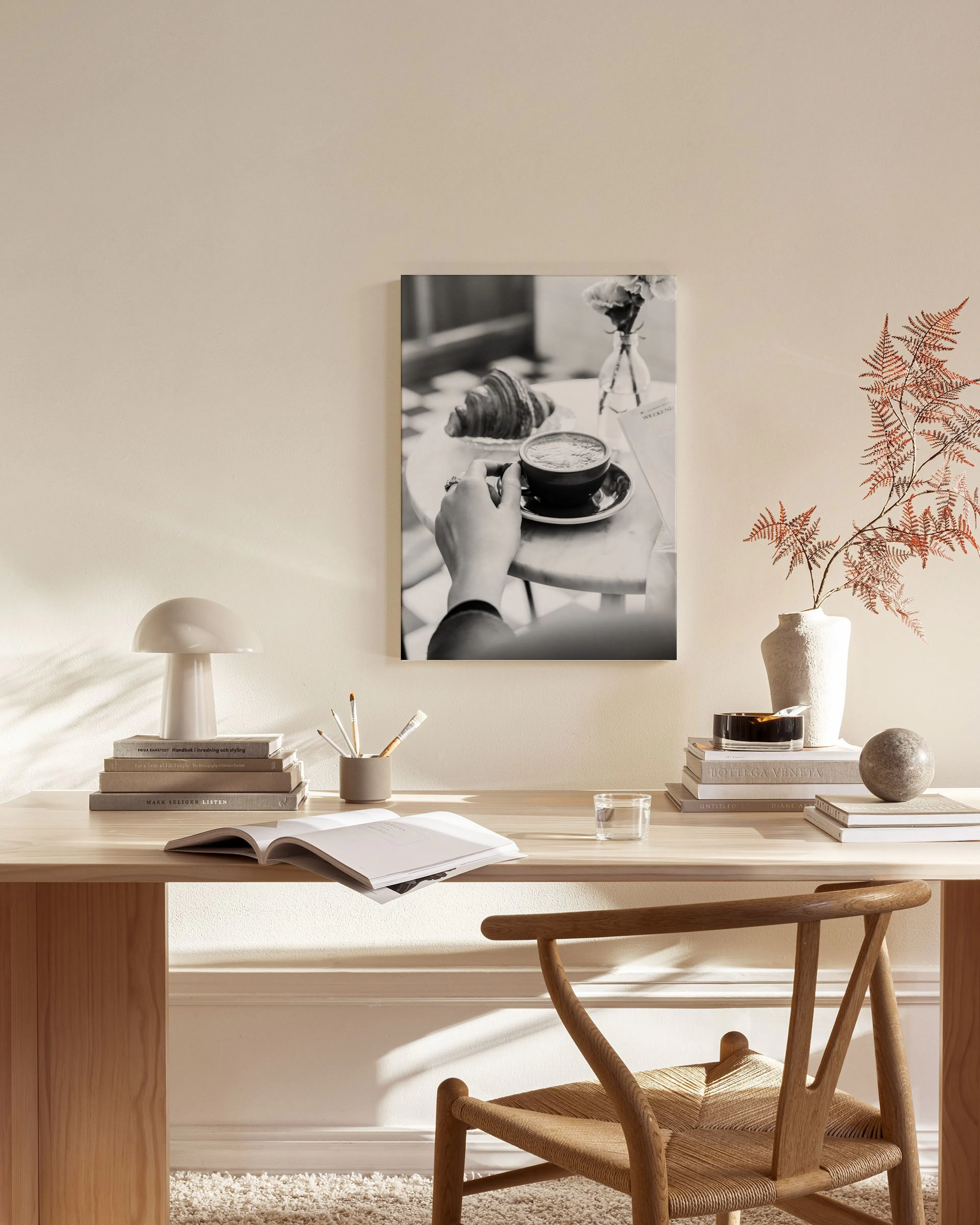 Toile noir et blanc dun café et croissant, tenue par une main, affichée dans un salon moderne et lumineux.