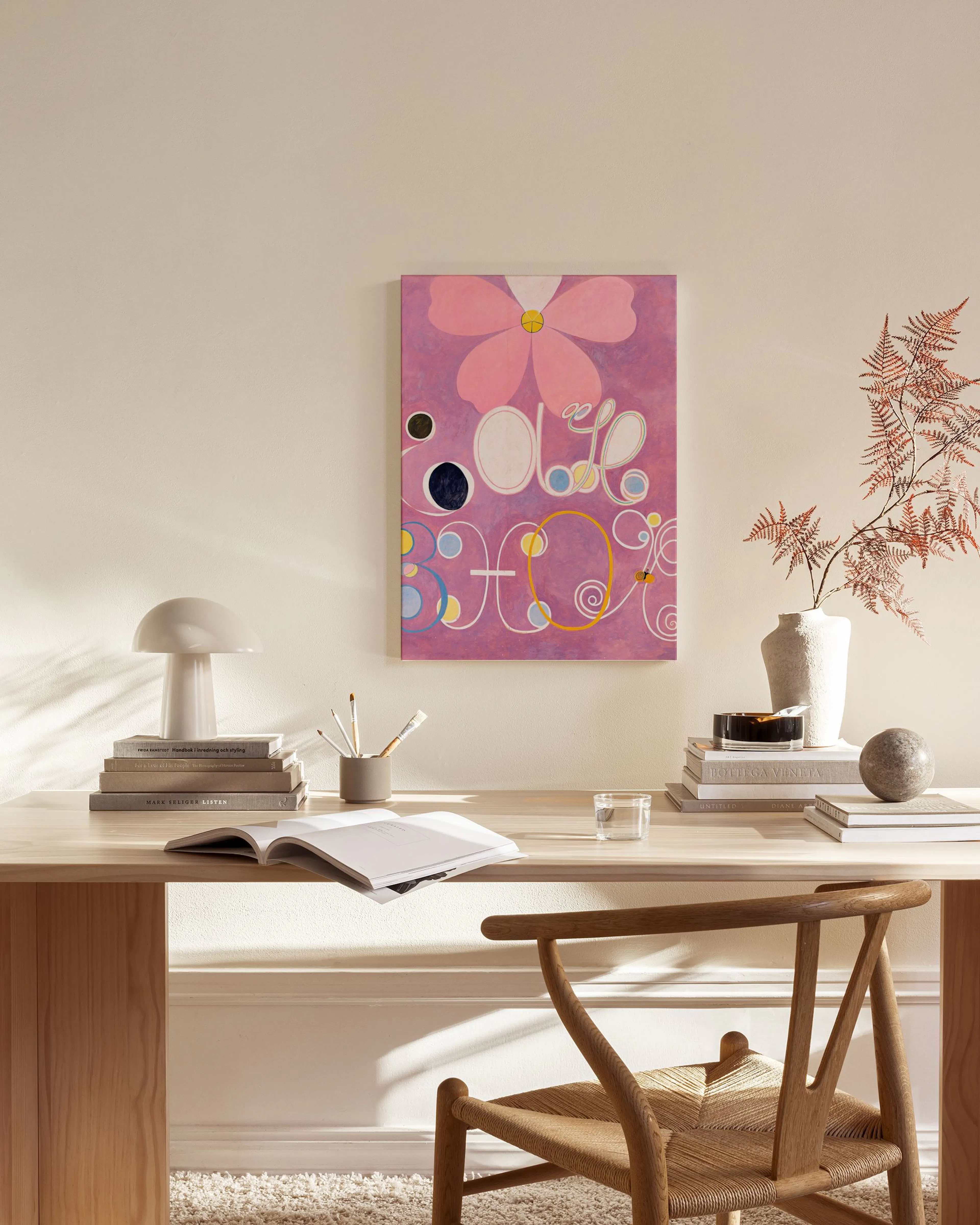 Leinwandbild mit rosa Blume und abstrakten Formen in Lila, Weiß, Gelb und Blau, hängend in einem hellen Wohnzimmer über einem Ho