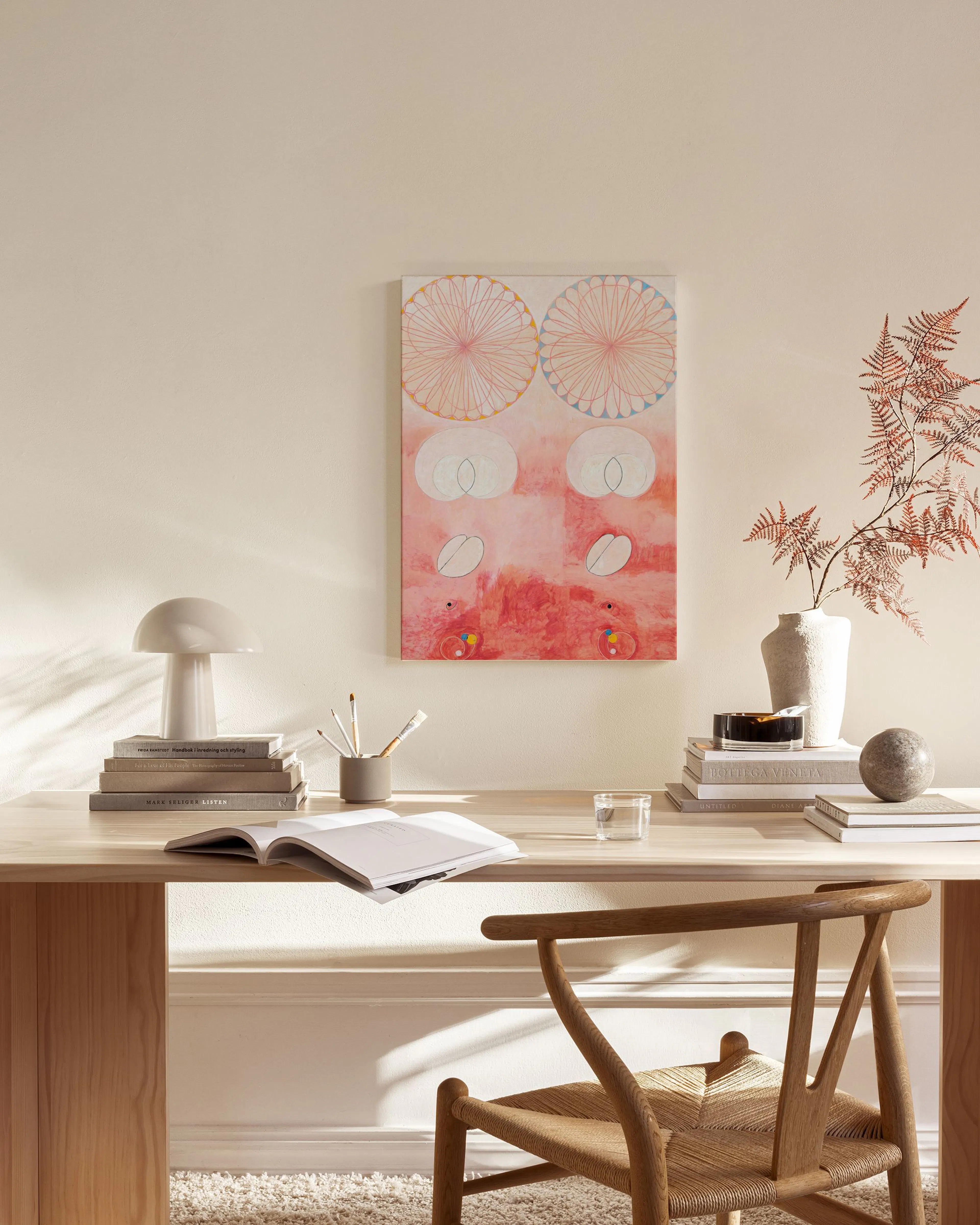 Ein Leinwandbild mit abstrakten Formen in Rosé- und Rottönen, umgeben von zwei großen, hellen Kreisen, an einer Wand in einem Wo