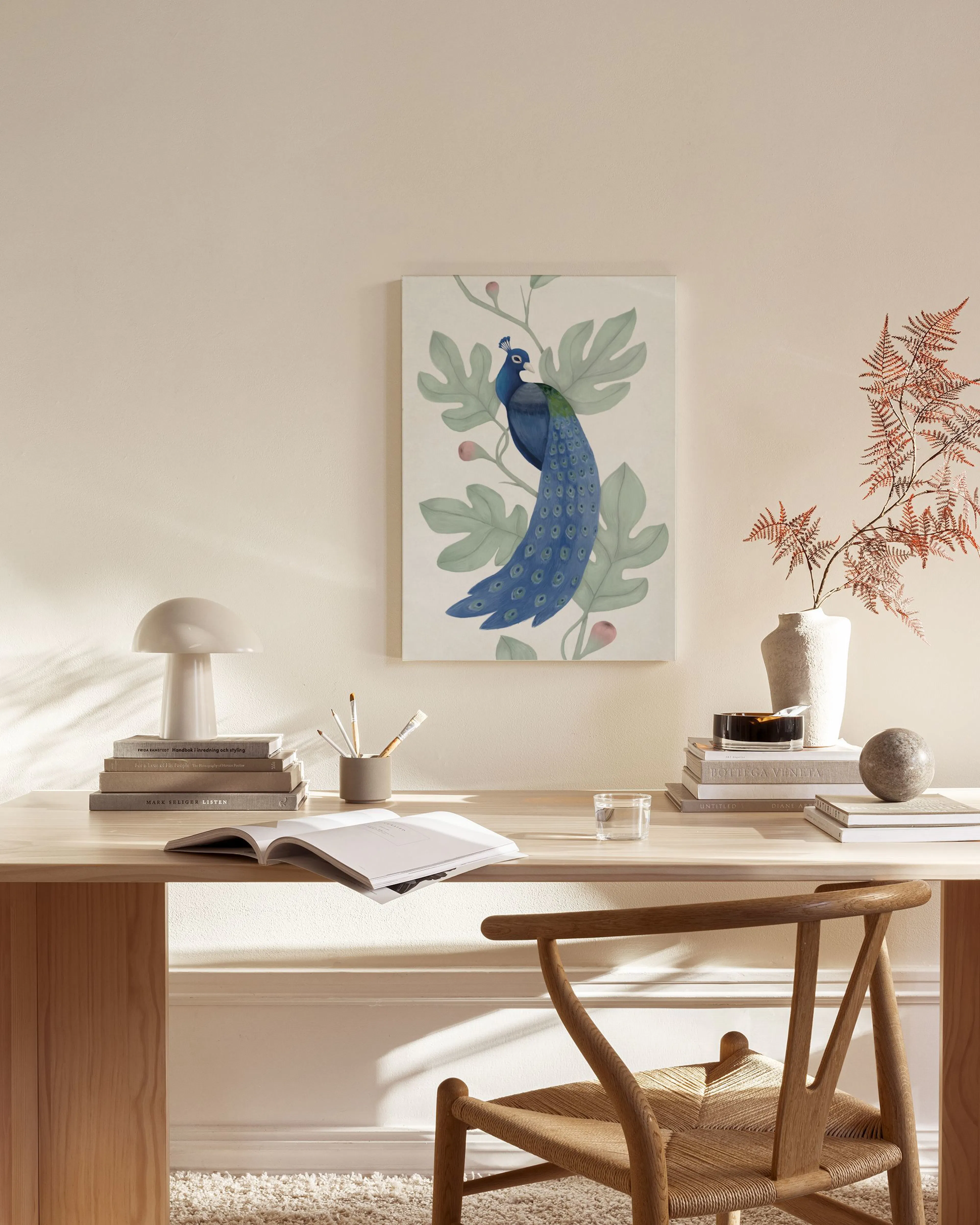 Obraz na plátne: modrý páv na vetve so zelenými listami a ružovými bobuľami, visí v obývačke nad drevenou komodou.