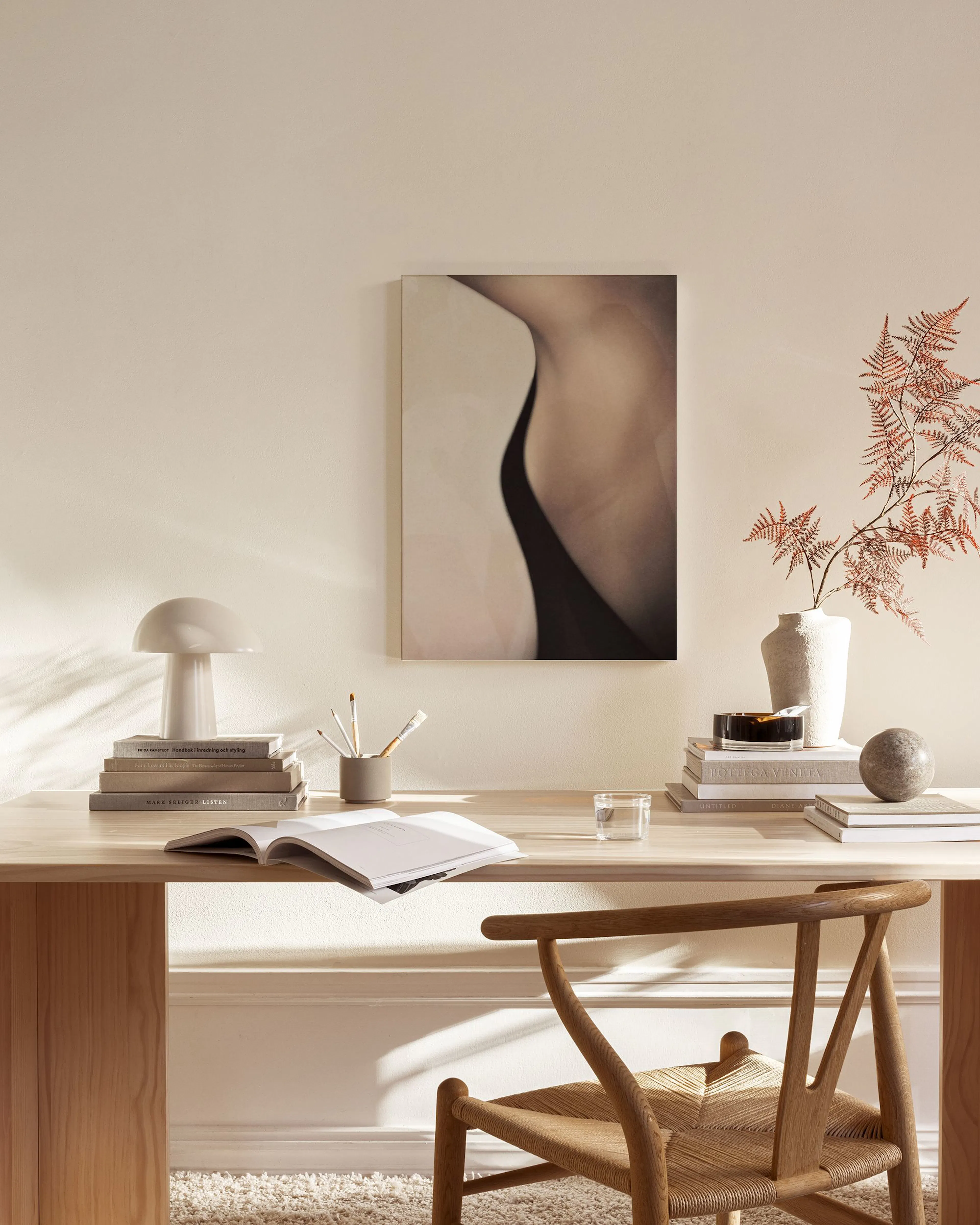 Lærred med en kunstnerisk gengivelse af en kvindekrop, der hænger i en moderne stue med en lænestol og sofabord.