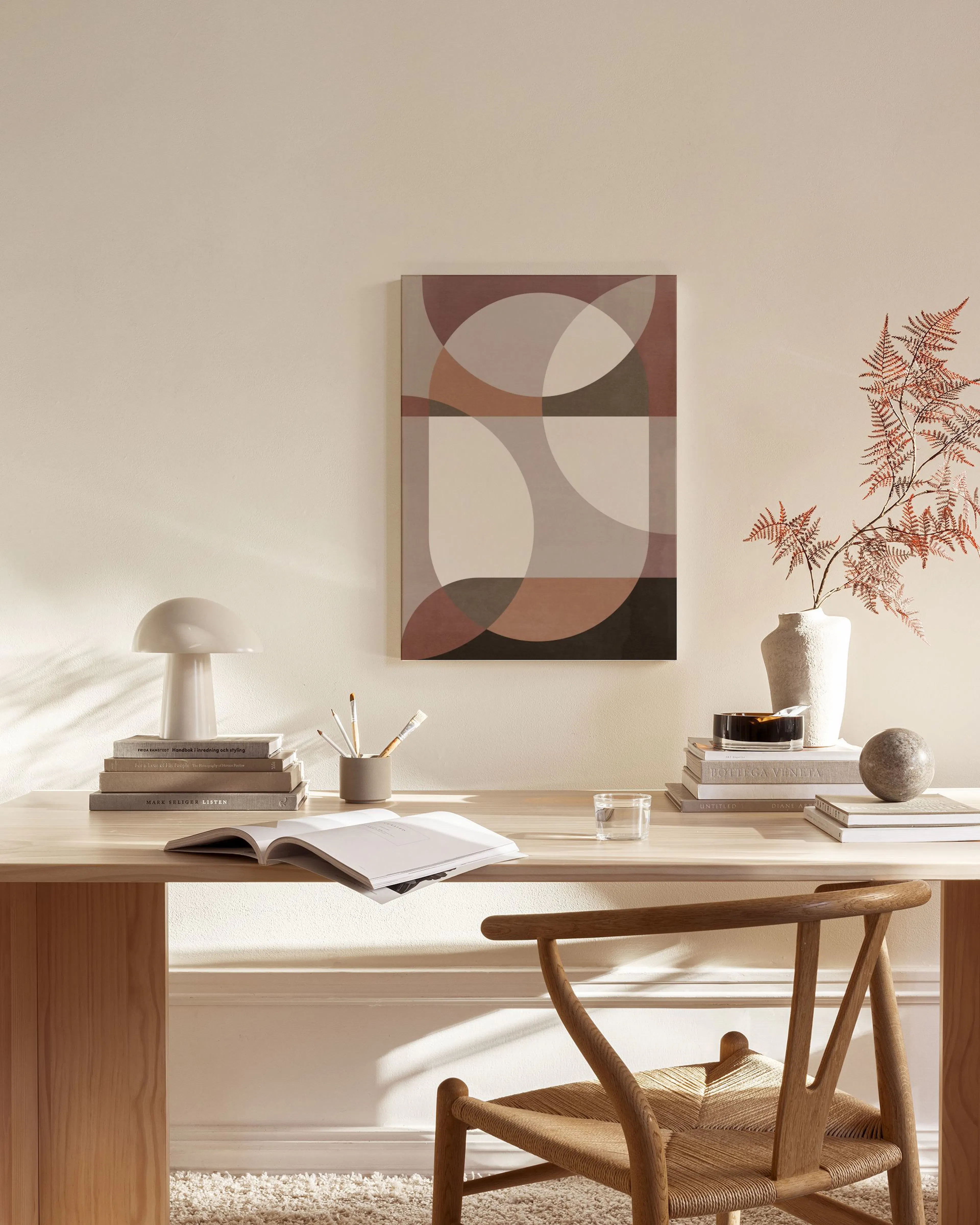 Abstract canvas print with geometric shapes in muted brown, grey, and cream tones, hanging in a minimalist living room.