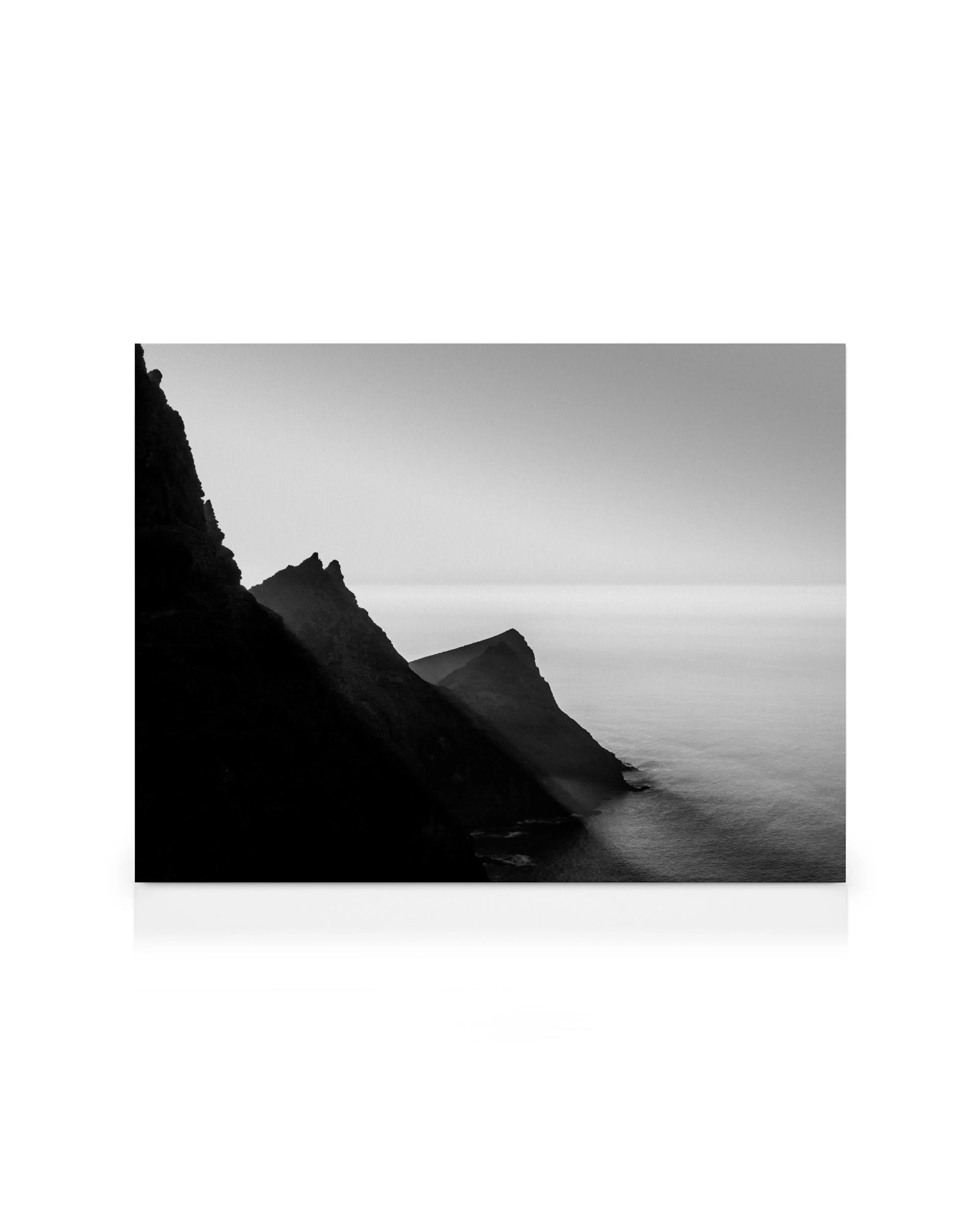 Schwarz-Weiß-Leinwandbild einer zerklüfteten Küste mit steilen Klippen und ruhigem Meer, das sich bis zum Horizont erstreckt.