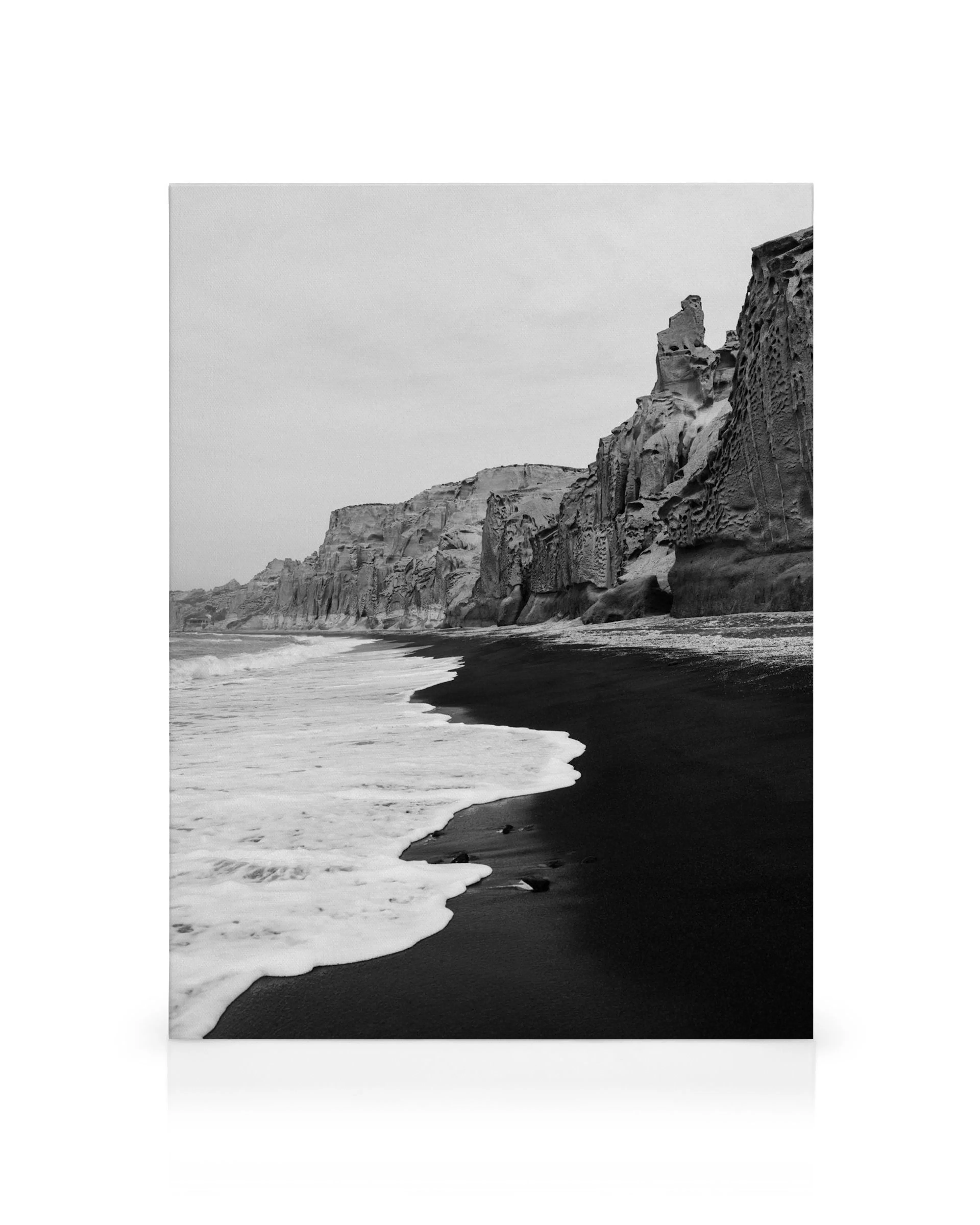 Black and white canvas print of a dark beach with white foamy waves and dramatic cliffs under a cloudy sky