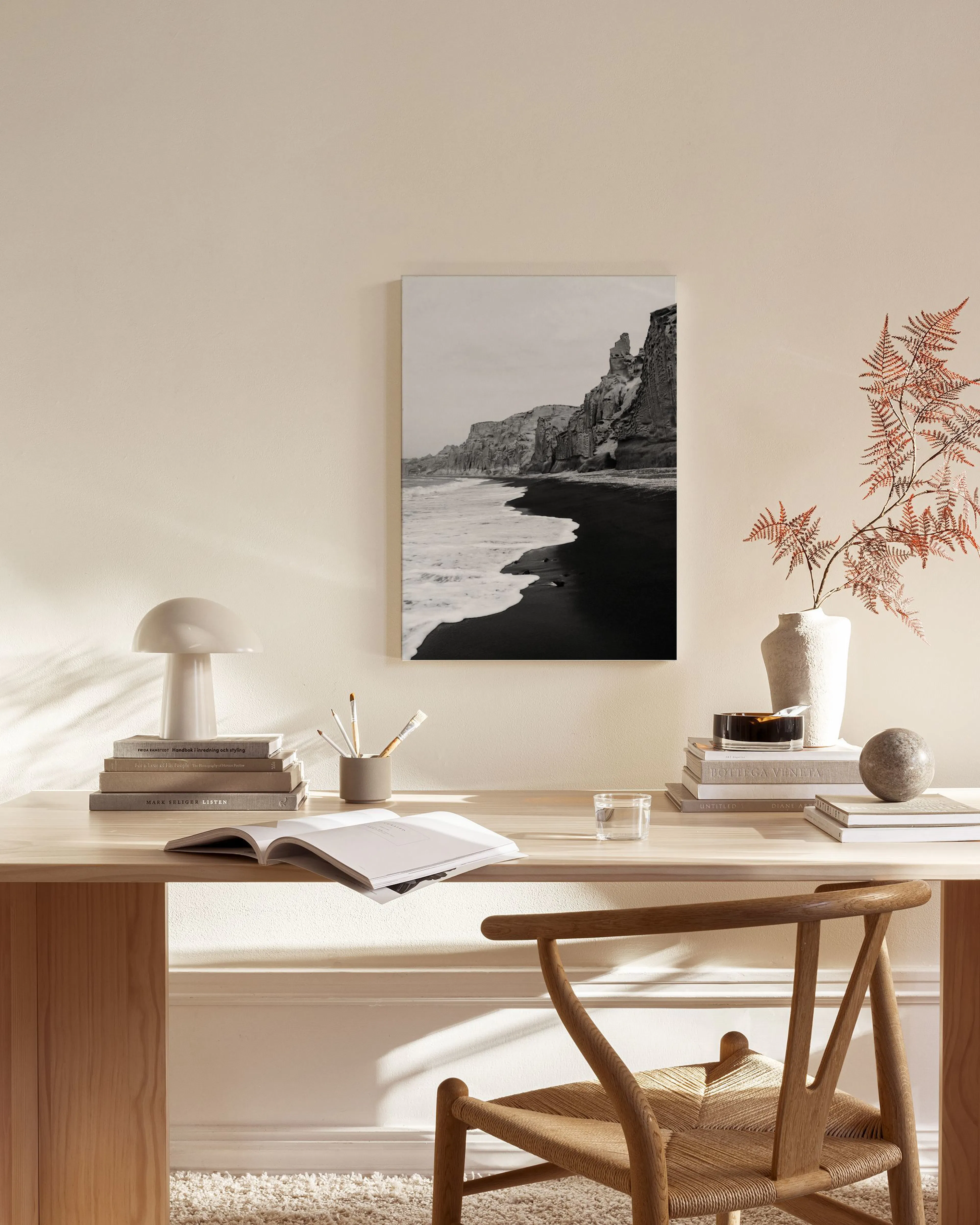 A black and white canvas print of a rocky coastline with ocean waves on a black sand beach, hanging in a minimalist living room.