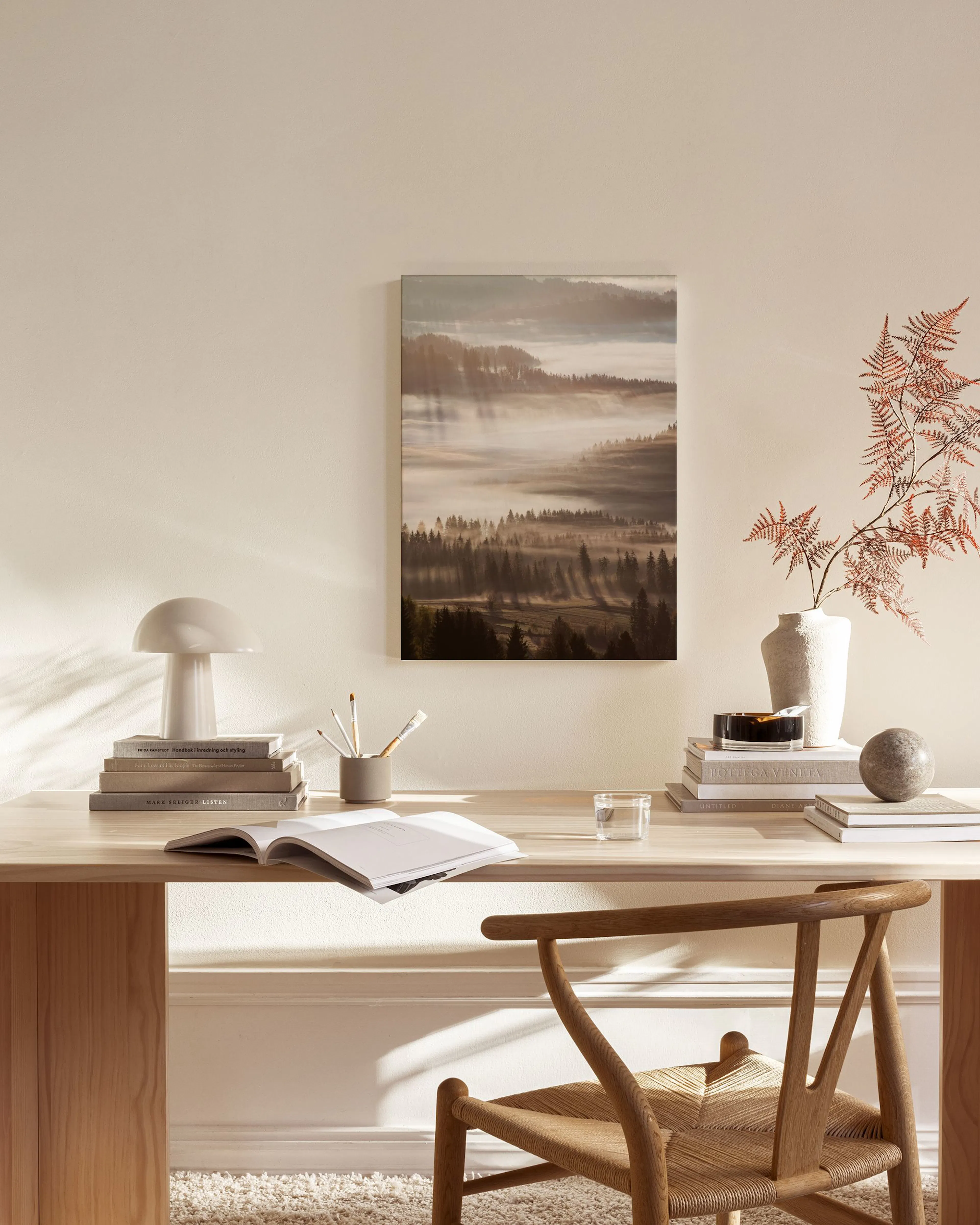 A canvas print of a misty forest valley with sun rays breaking through, hanging in a modern living room above a wooden console.