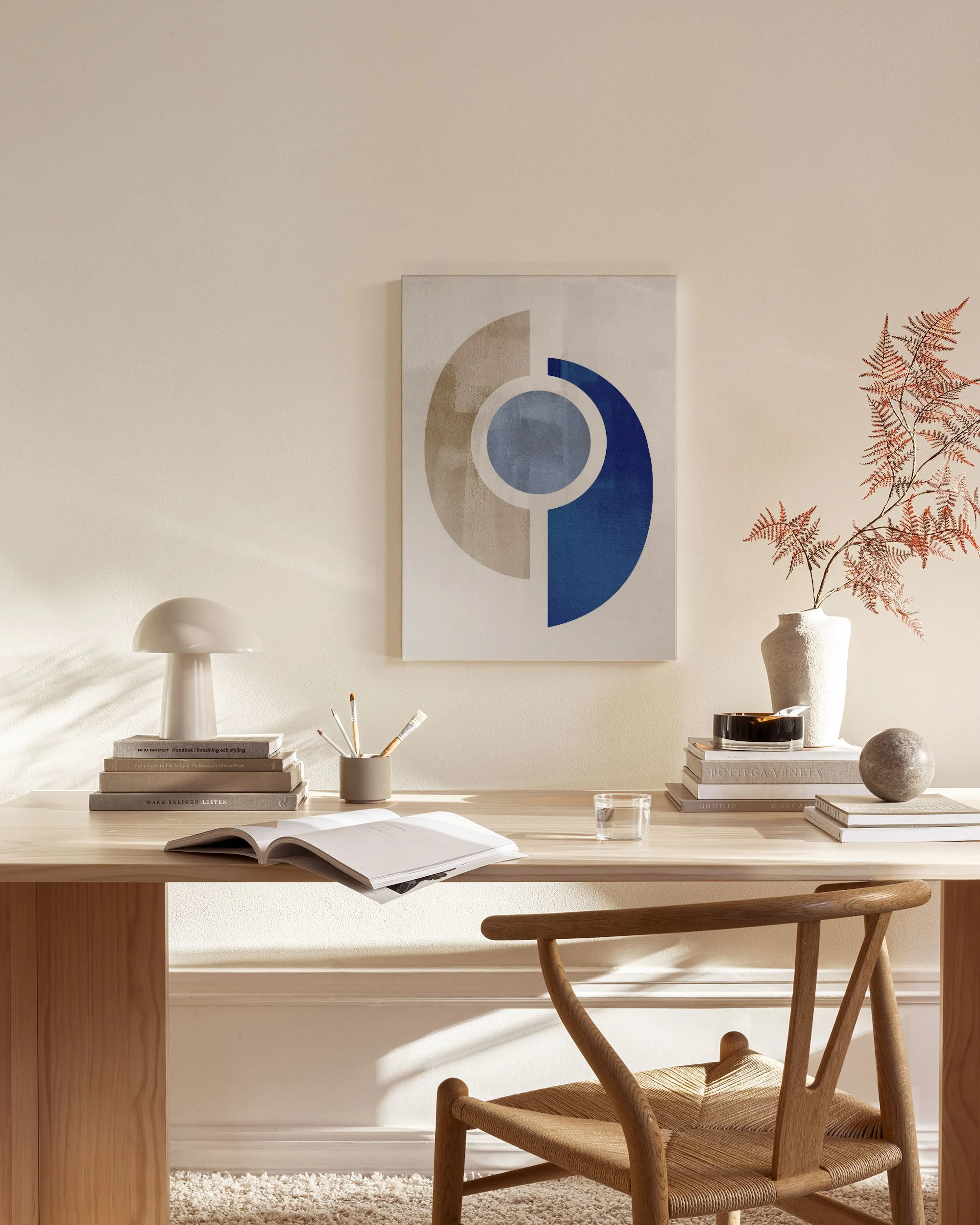 Lienzo abstracto con formas geométricas en tonos azul y beige, colgado sobre un mueble bajo en una sala moderna.