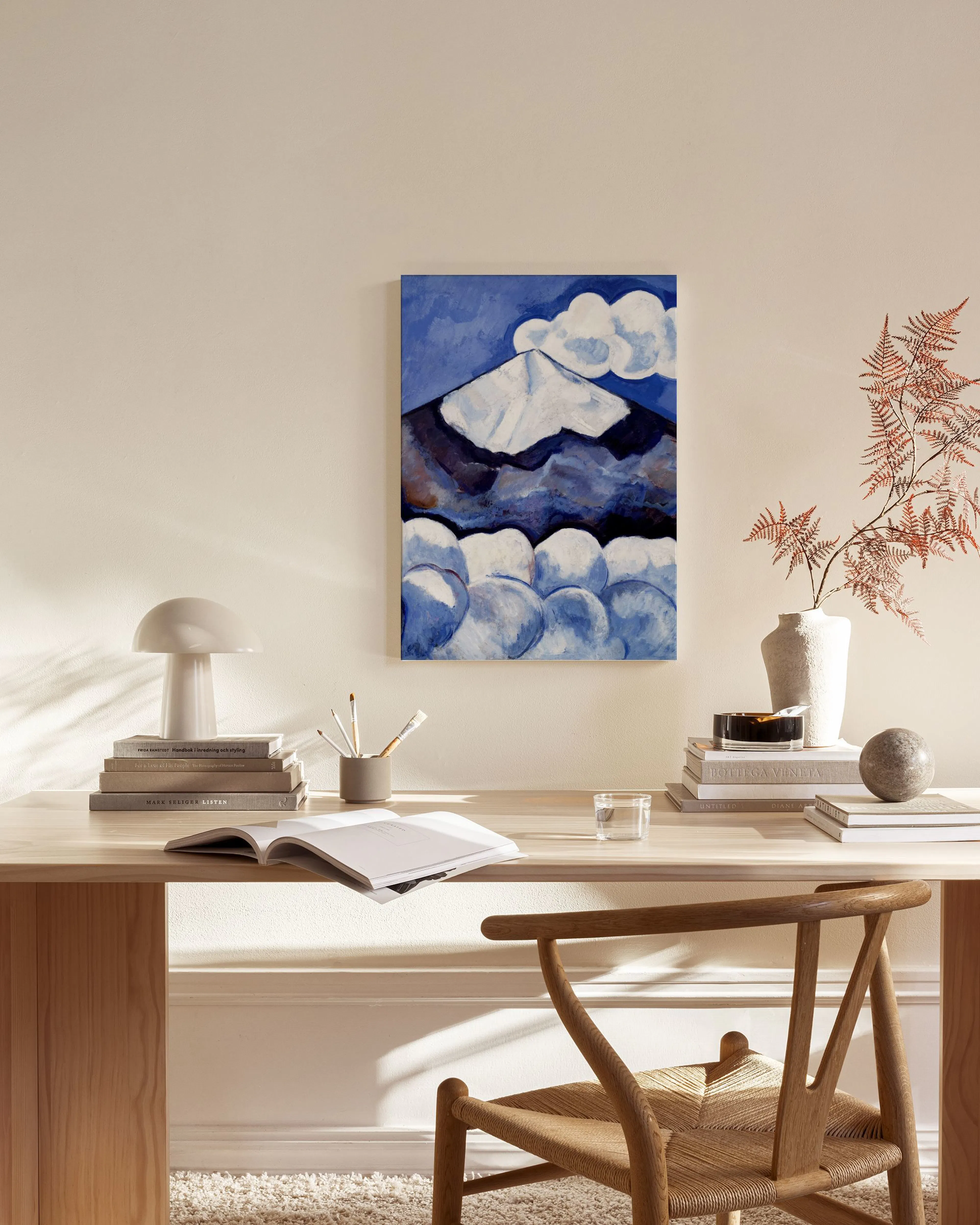 A canvas print of a blue and white abstract mountain with clouds, hanging above a wooden console table in a minimalist living ro
