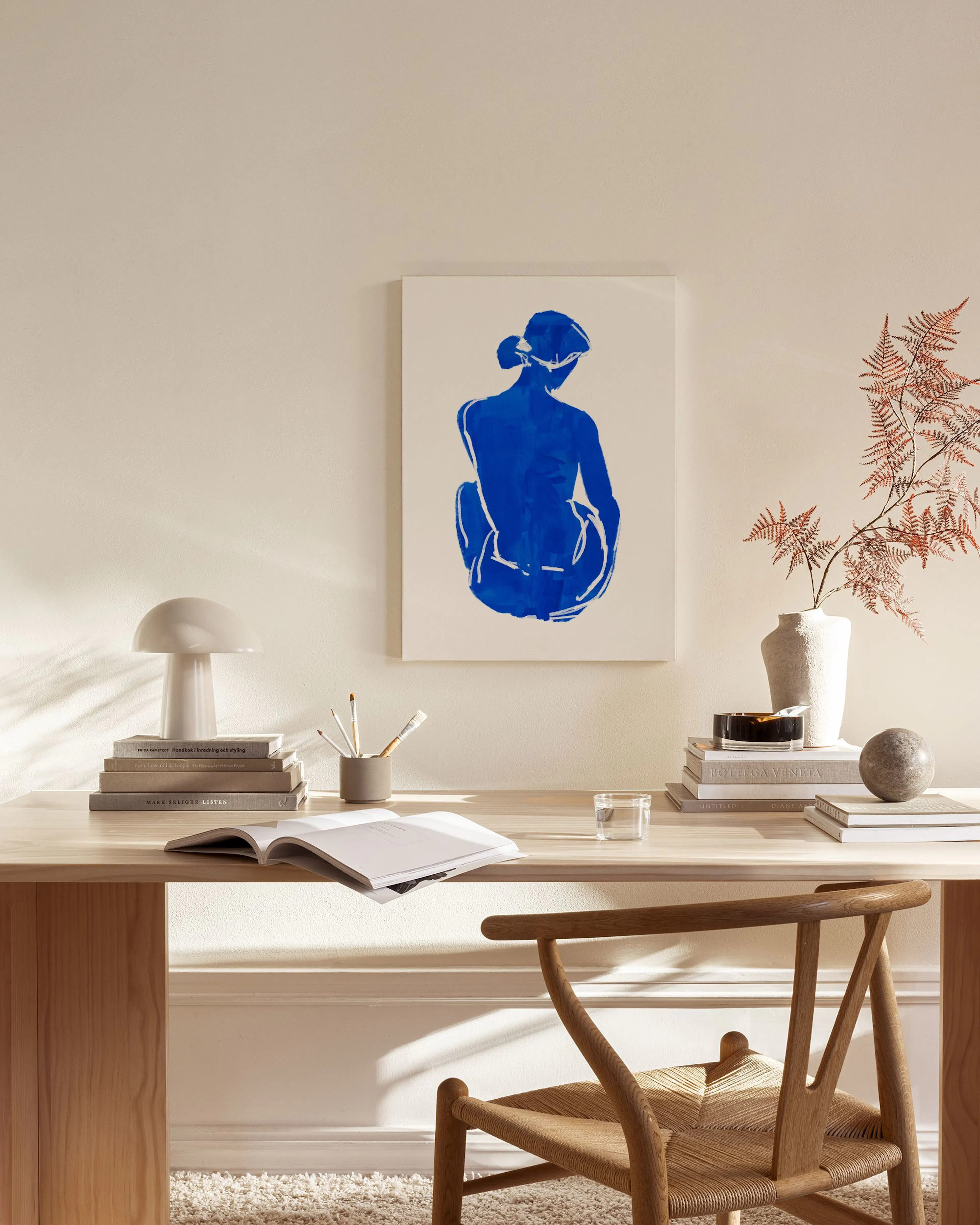Leinwandbild einer sitzenden Frau in leuchtendem Kobaltblau, hängend in einem hellen Wohnzimmer über einem Sideboard.
