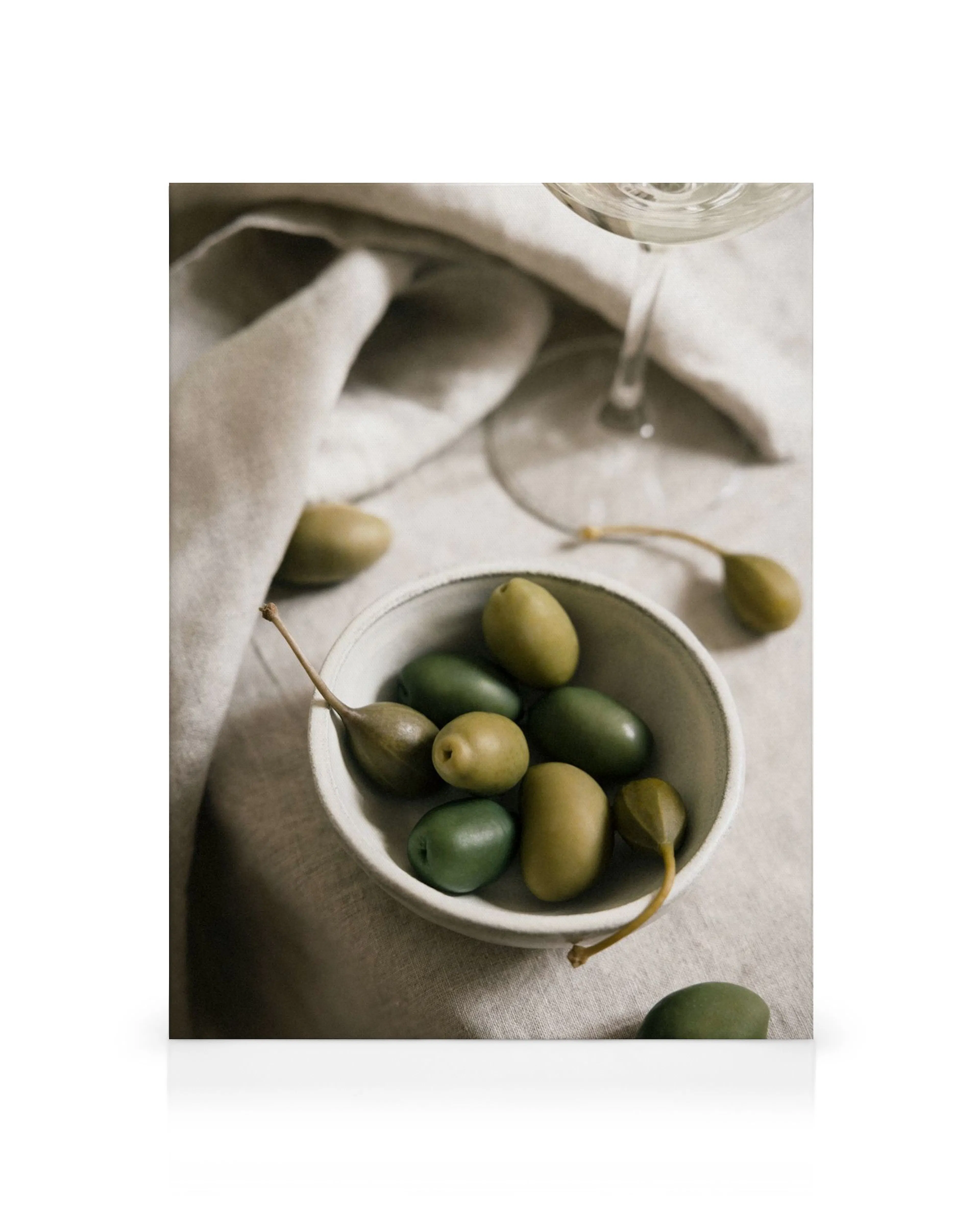 Toile de nature morte avec des olives vertes et des câpres dans un bol, avec un verre de vin blanc sur une nappe beige.