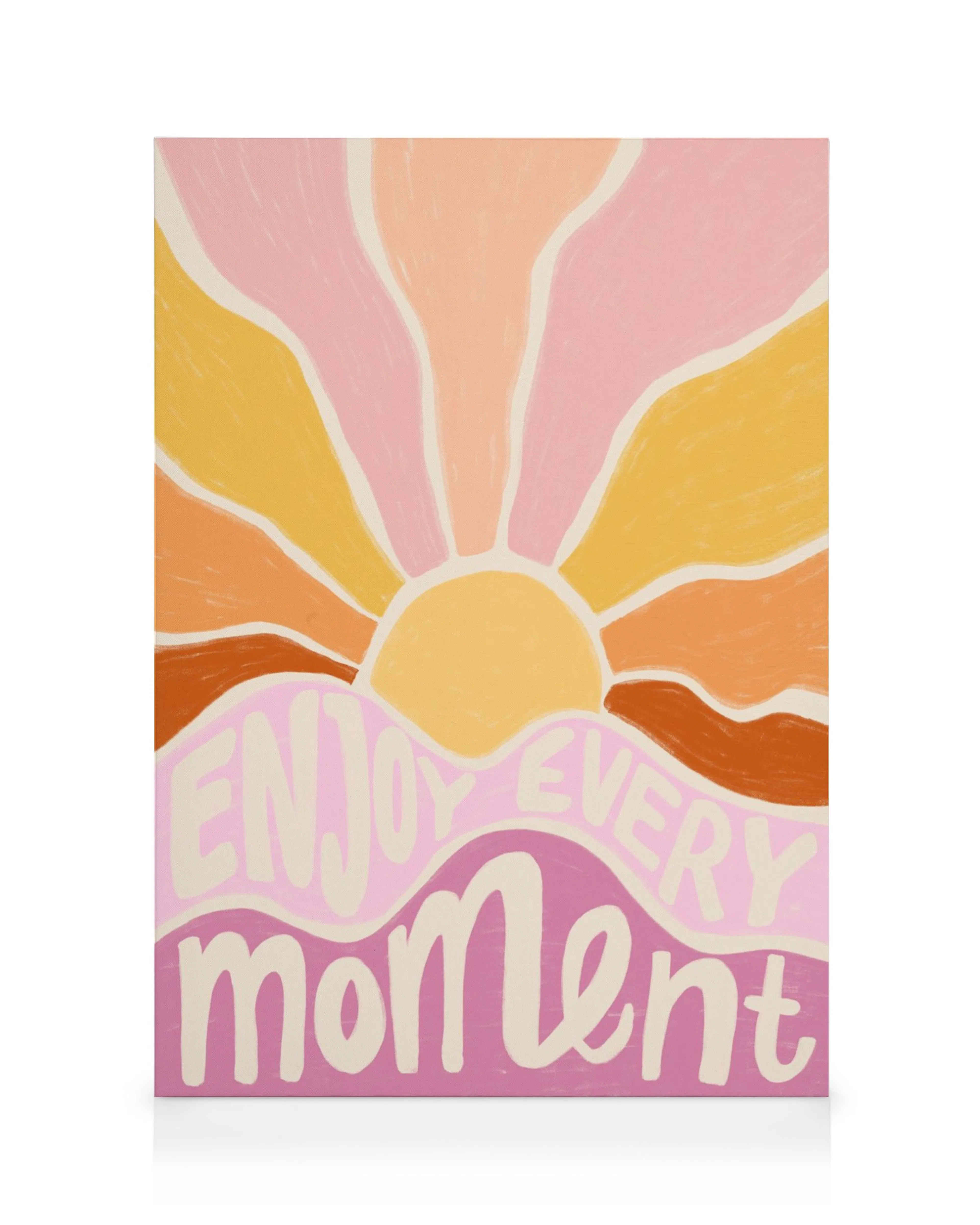 A canvas print featuring a vibrant sunset with Enjoy Every Moment in pink text on a light pink background.