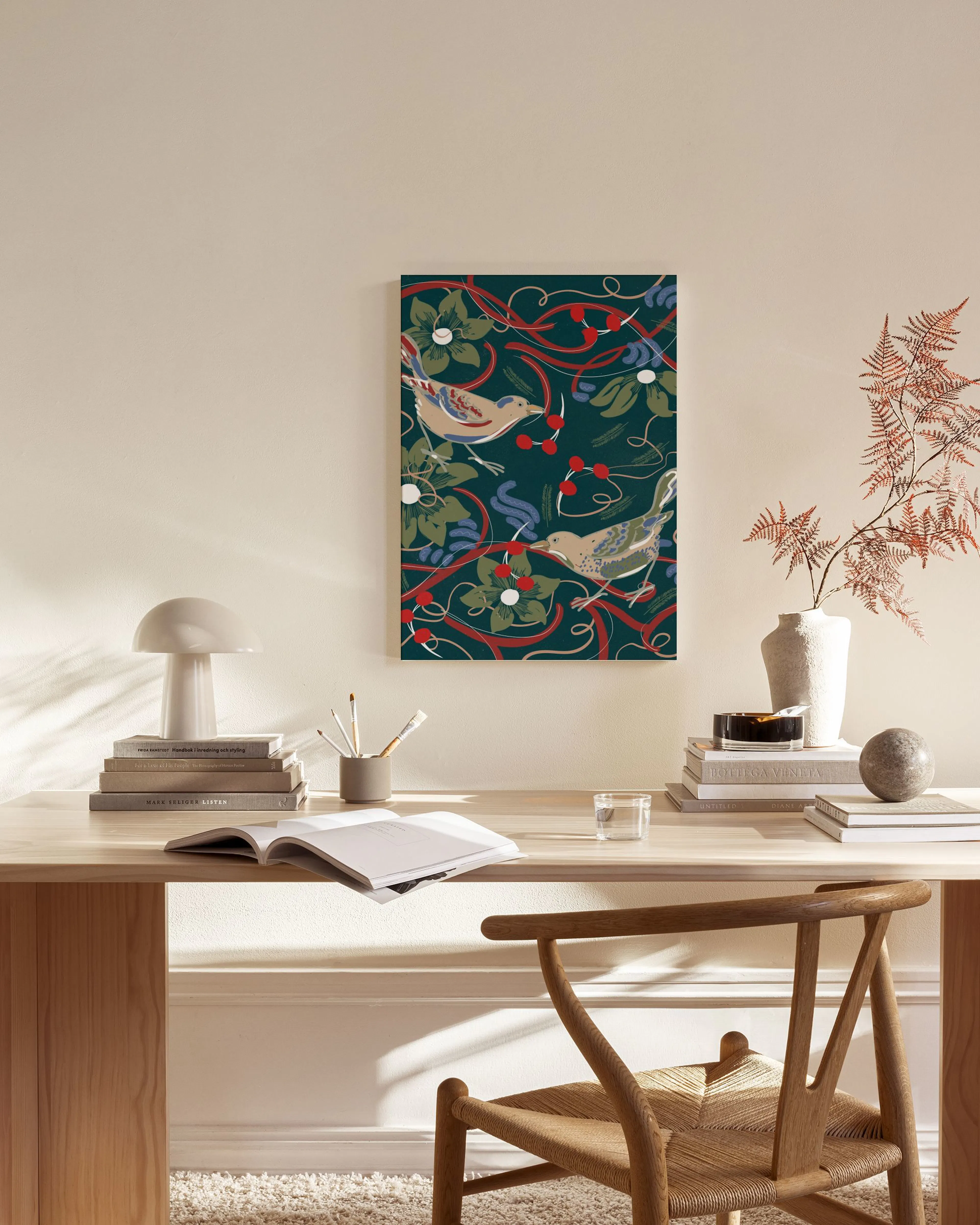 A canvas print of a bird and botanical pattern with berries and leaves on a dark teal background, hanging in a minimalist living