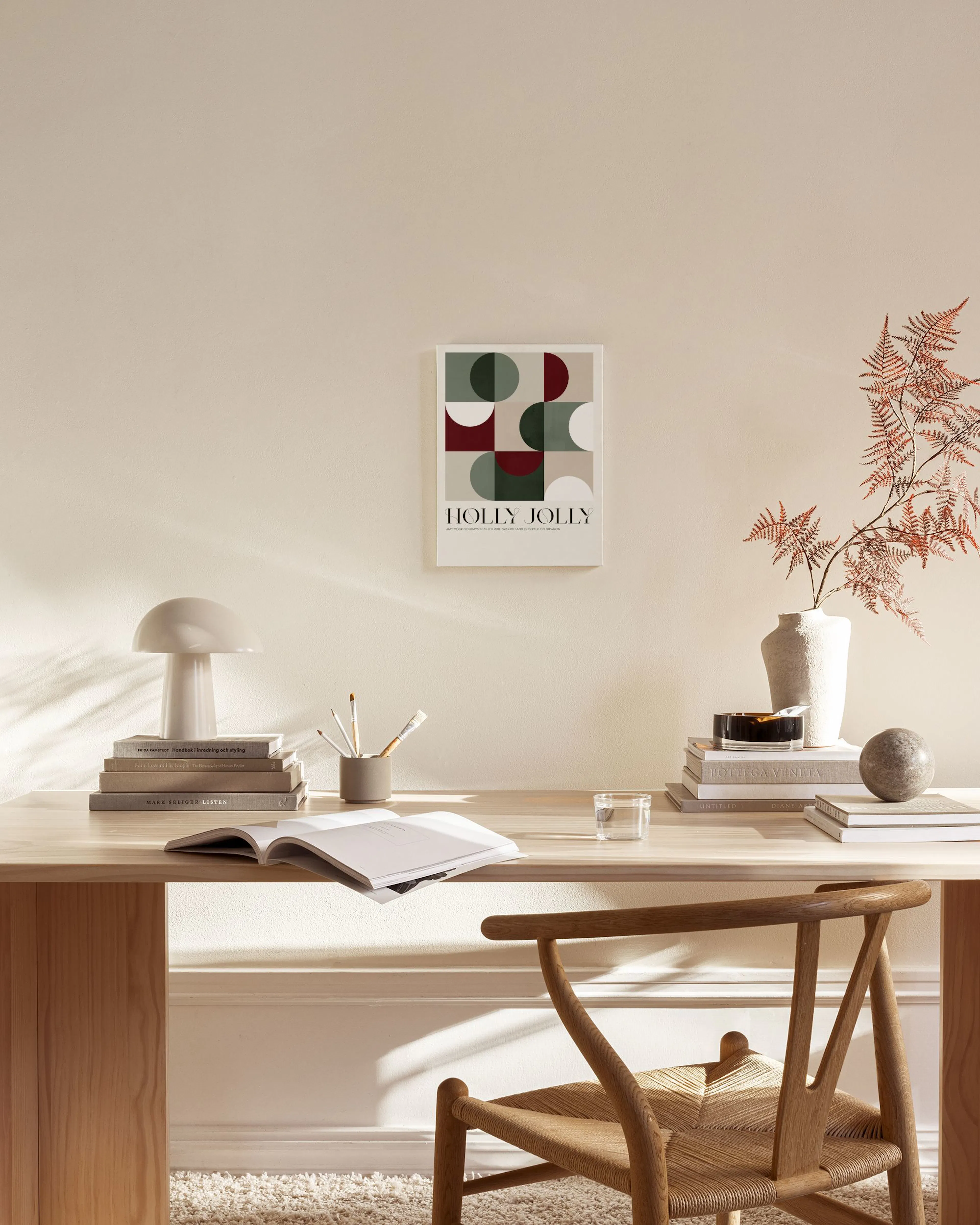 A canvas print with abstract green, red, and beige geometric shapes and “HOLLY JOLLY” text, hanging in a bright living room.