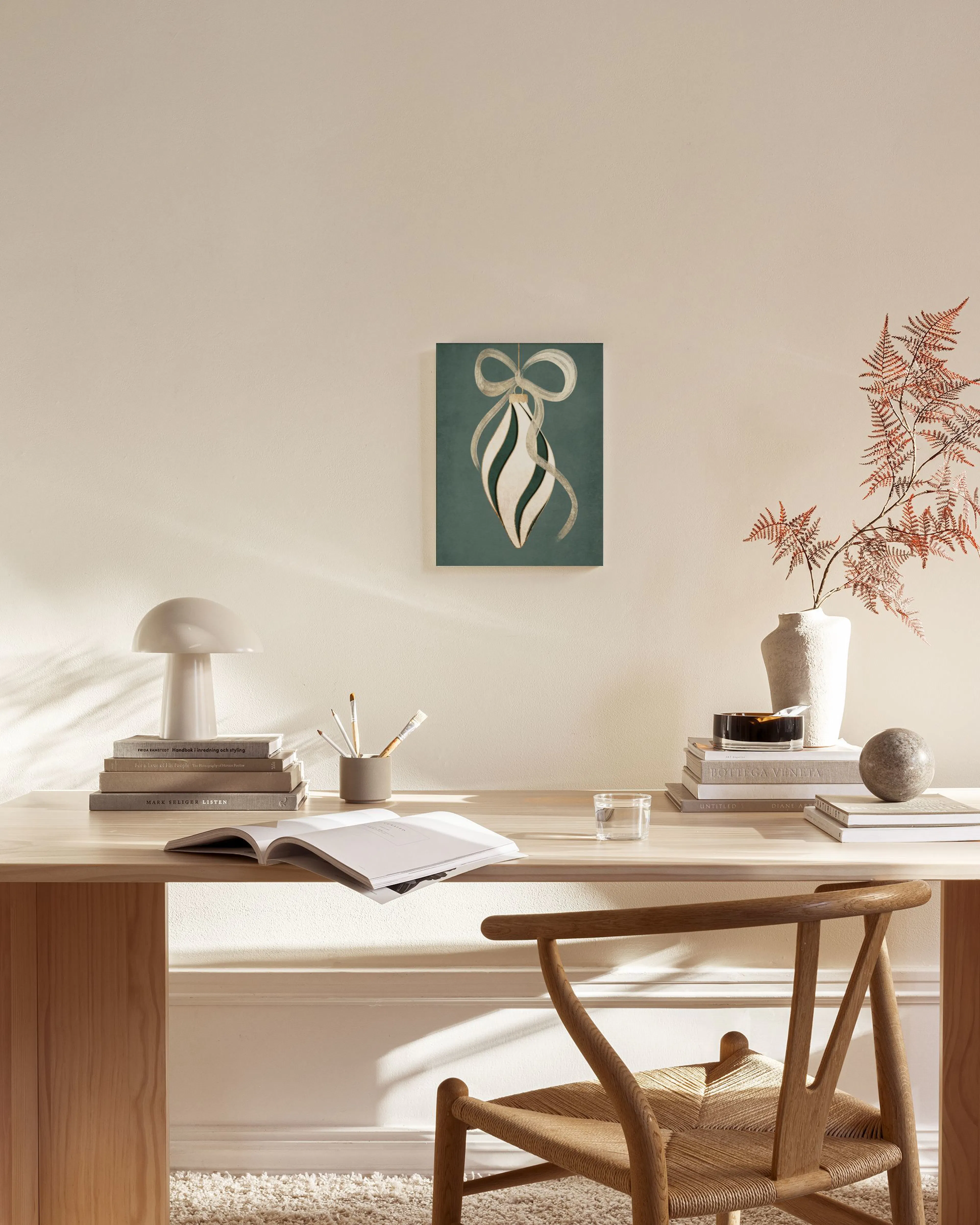 A canvas print of a green Christmas bauble with a beige ribbon and white swirl, hanging in a bright living room.