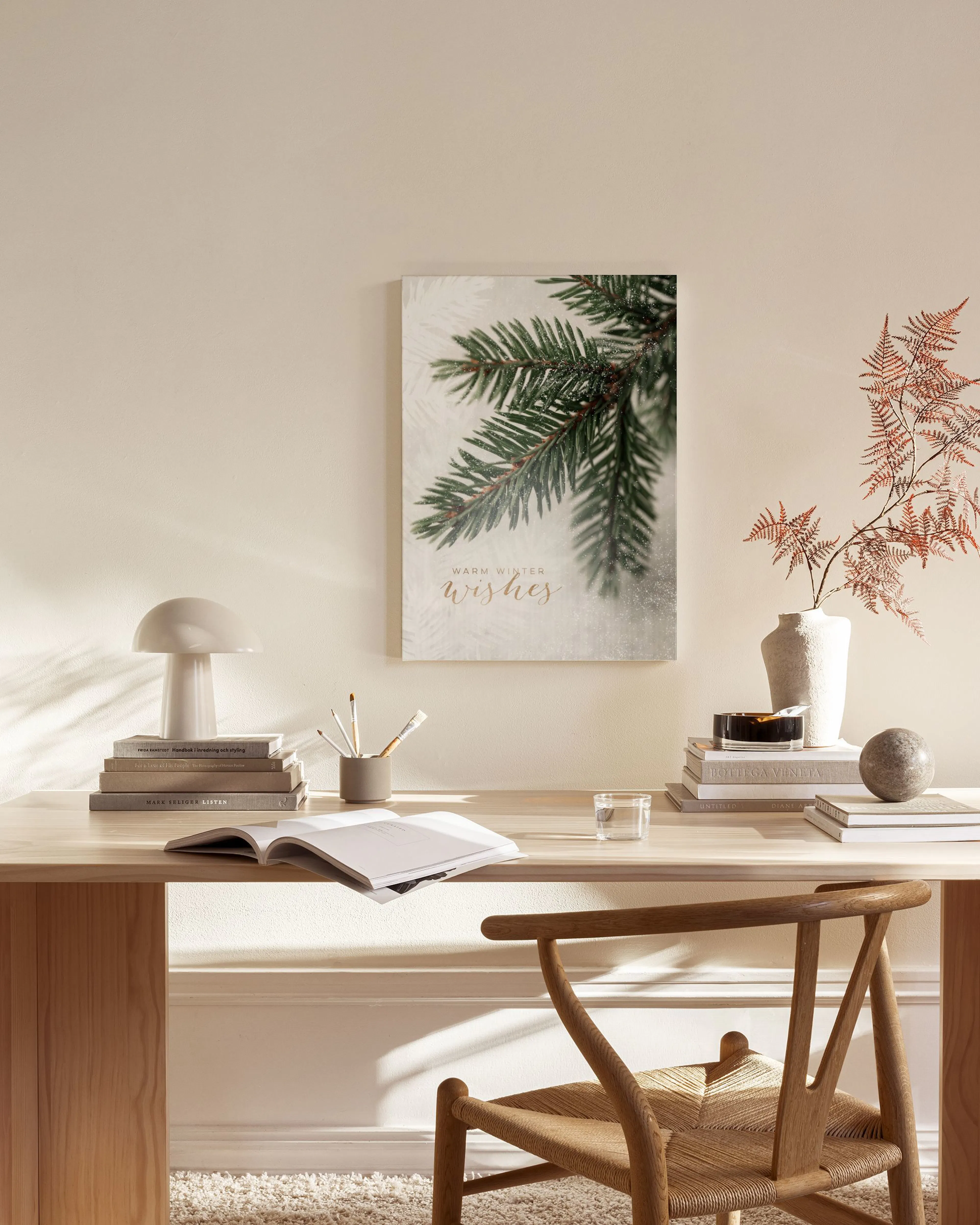 A canvas print of a green pine branch with Warm Winter Wishes in gold script, hanging in a modern living room.