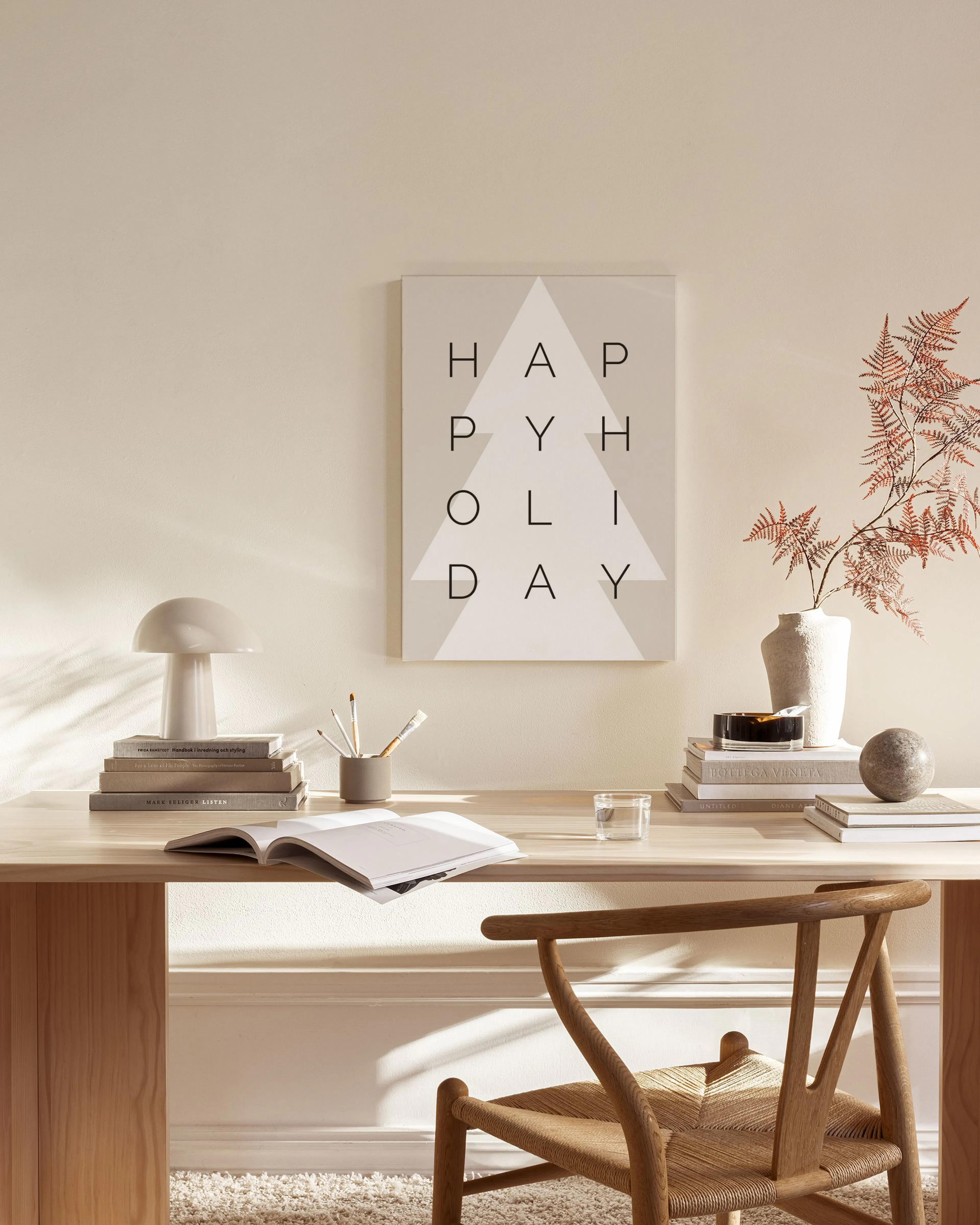 A canvas print with HAPPY HOLIDAY text and a white geometric Christmas tree, hanging in a neutral living room.